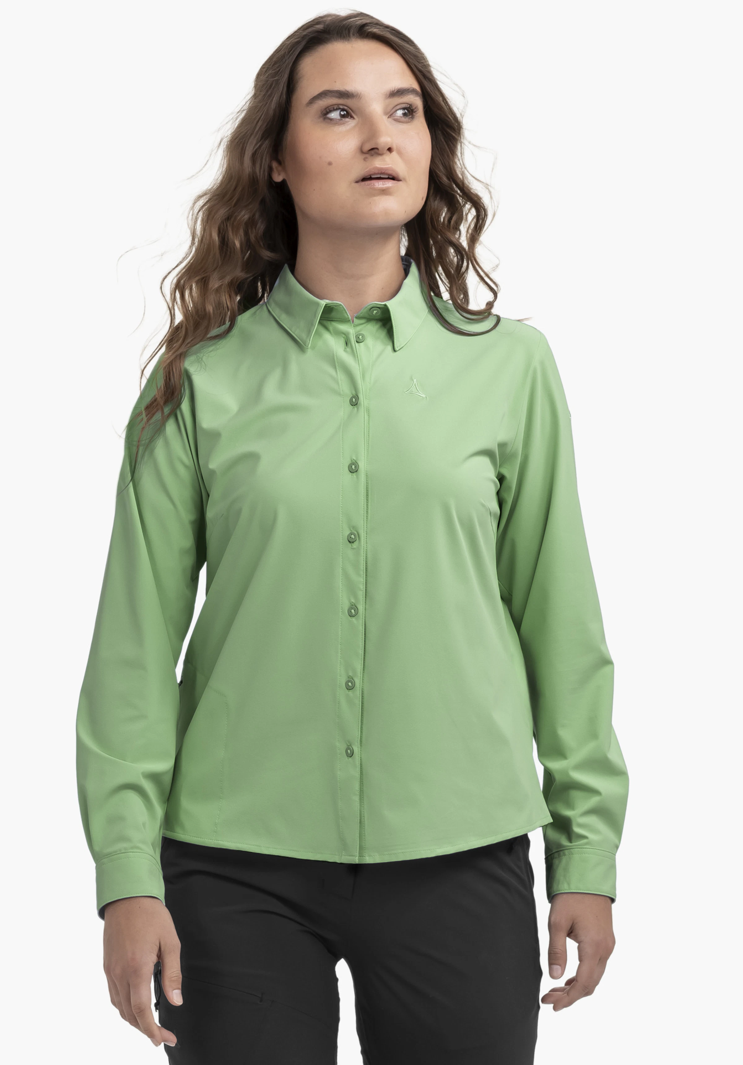 Blouse Style Dunajec WMN in het groen. Het model staat in vooraanzicht en draagt de blouse met lange mouwen en subtiel Schöffel-logo op de linkerborst, afgebeeld tegen een neutrale achtergrond.