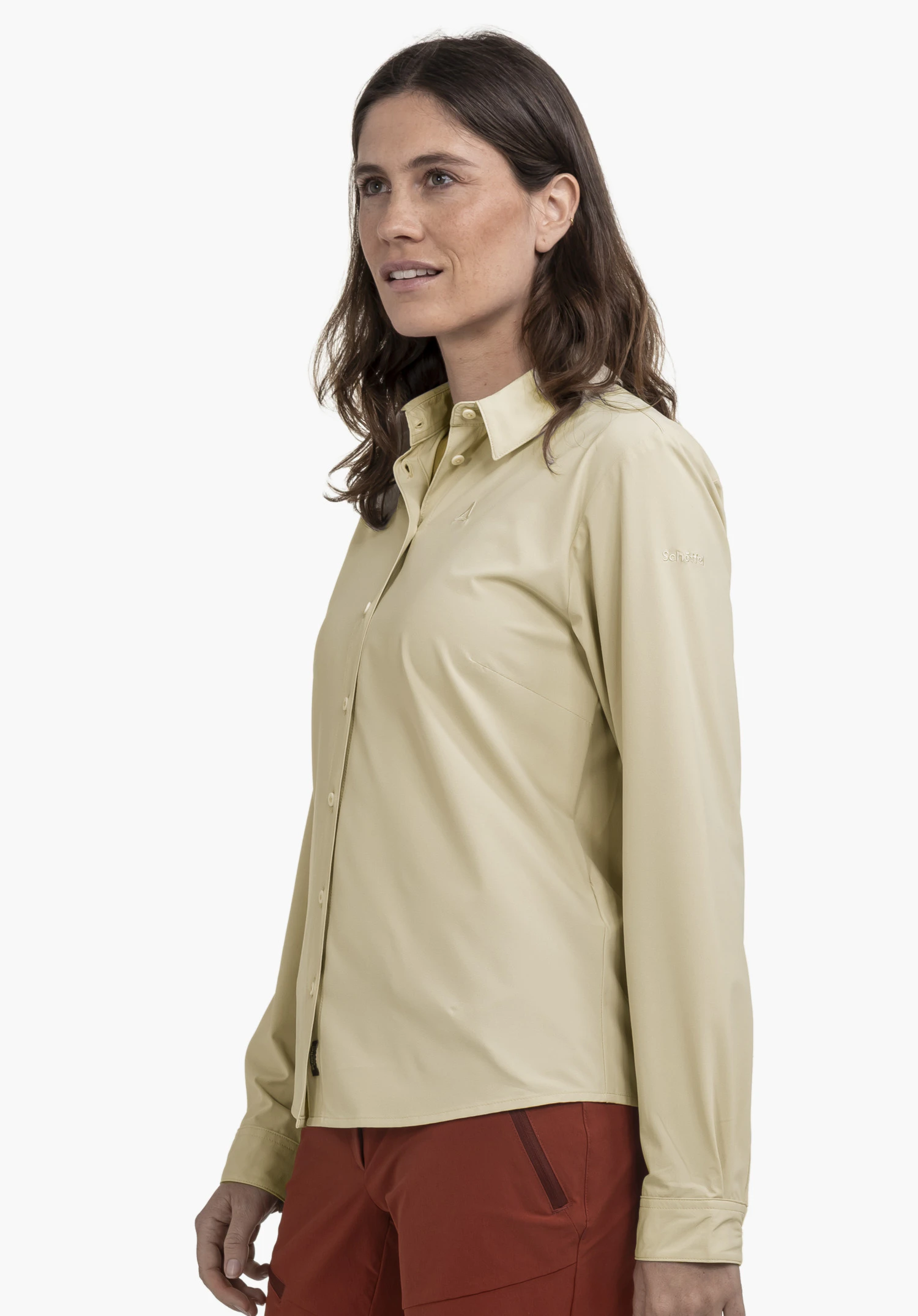 Blouse Style Dunajec WMN en beige. Le mannequin se tient de profil devant un fond neutre pour présenter la blouse. Le logo Schöffel discret est visible sur la manche.