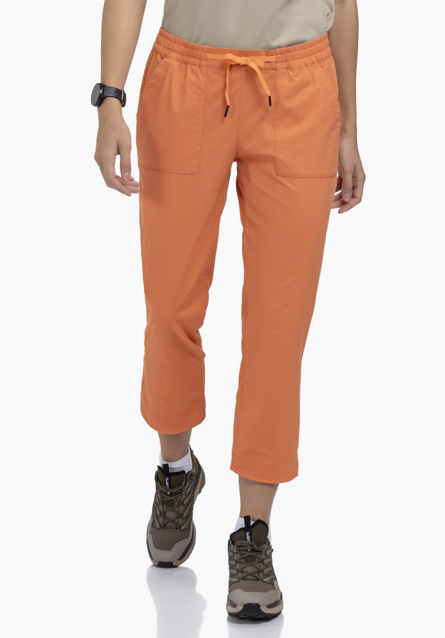 Pants Rangun L en orange, porté par un mannequin de face. Le mannequin fait un pas en avant et présente le pantacourt avec un cordon de serrage noué à la taille sur un fond neutre.