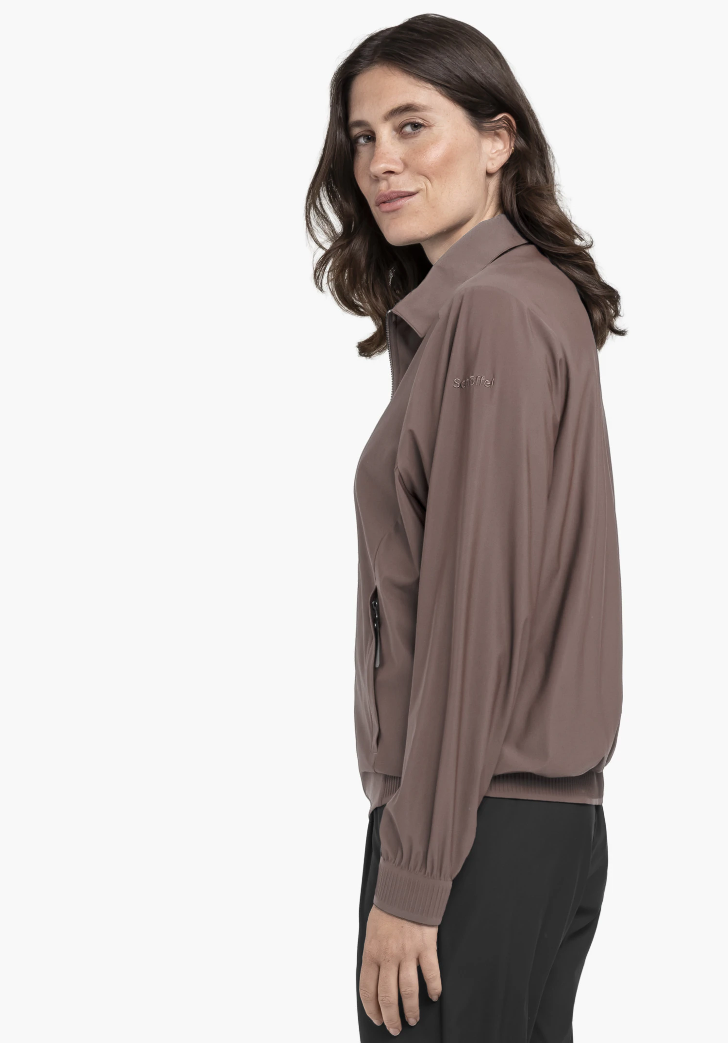 Jersey Jk Style Calmay WMN en marron. On y voit un modèle qui se tient de profil et porte la veste avec le logo Schöffel bien visible sur la manche gauche, présenté devant un fond neutre.