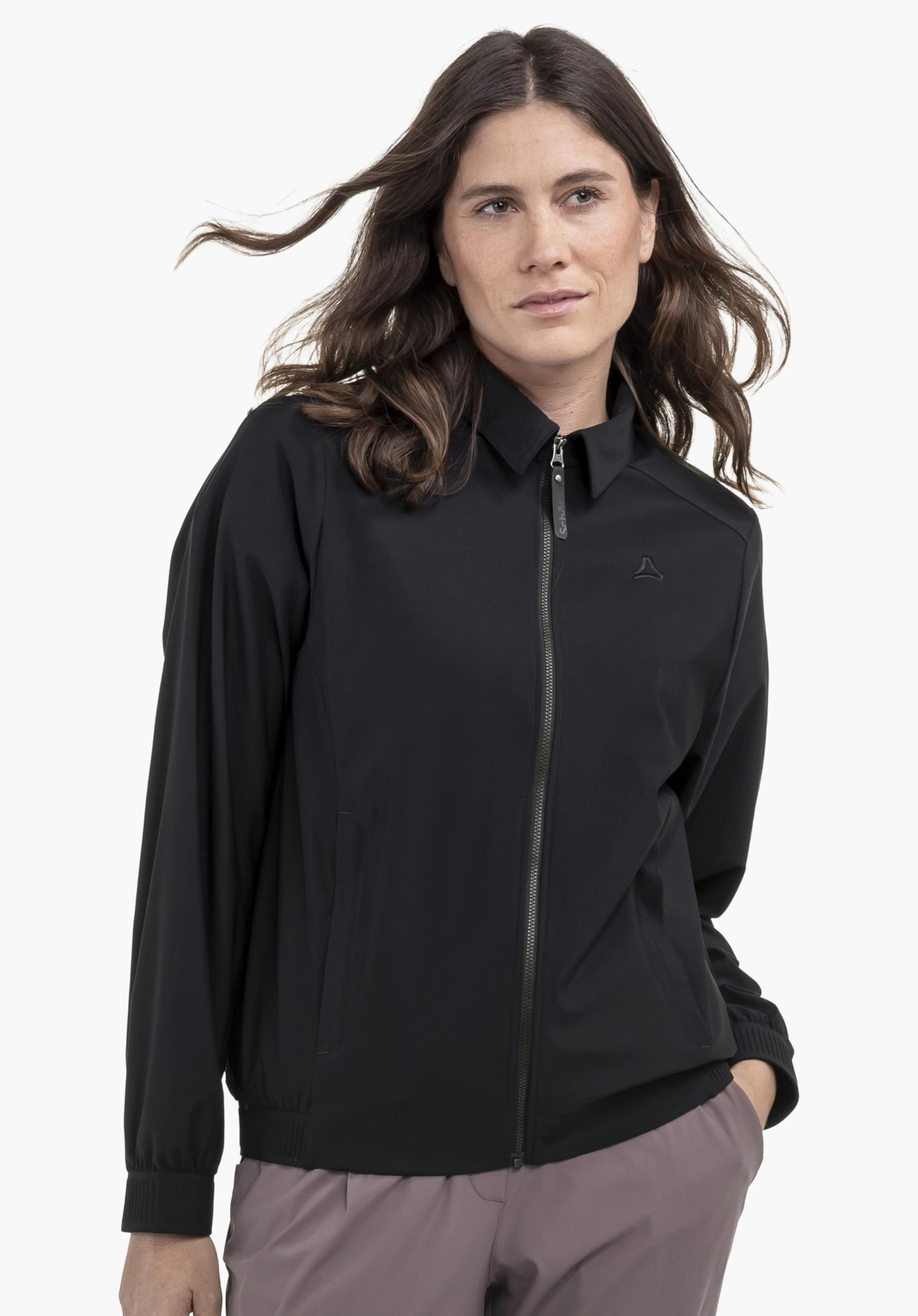 Jersey Jk Style Calmay WMN en noir. Un modèle est présenté de face sur un fond neutre, ses cheveux bougeant légèrement au gré du vent. Le logo Schöffel discrètement placé sur la poitrine souligne le design minimaliste.