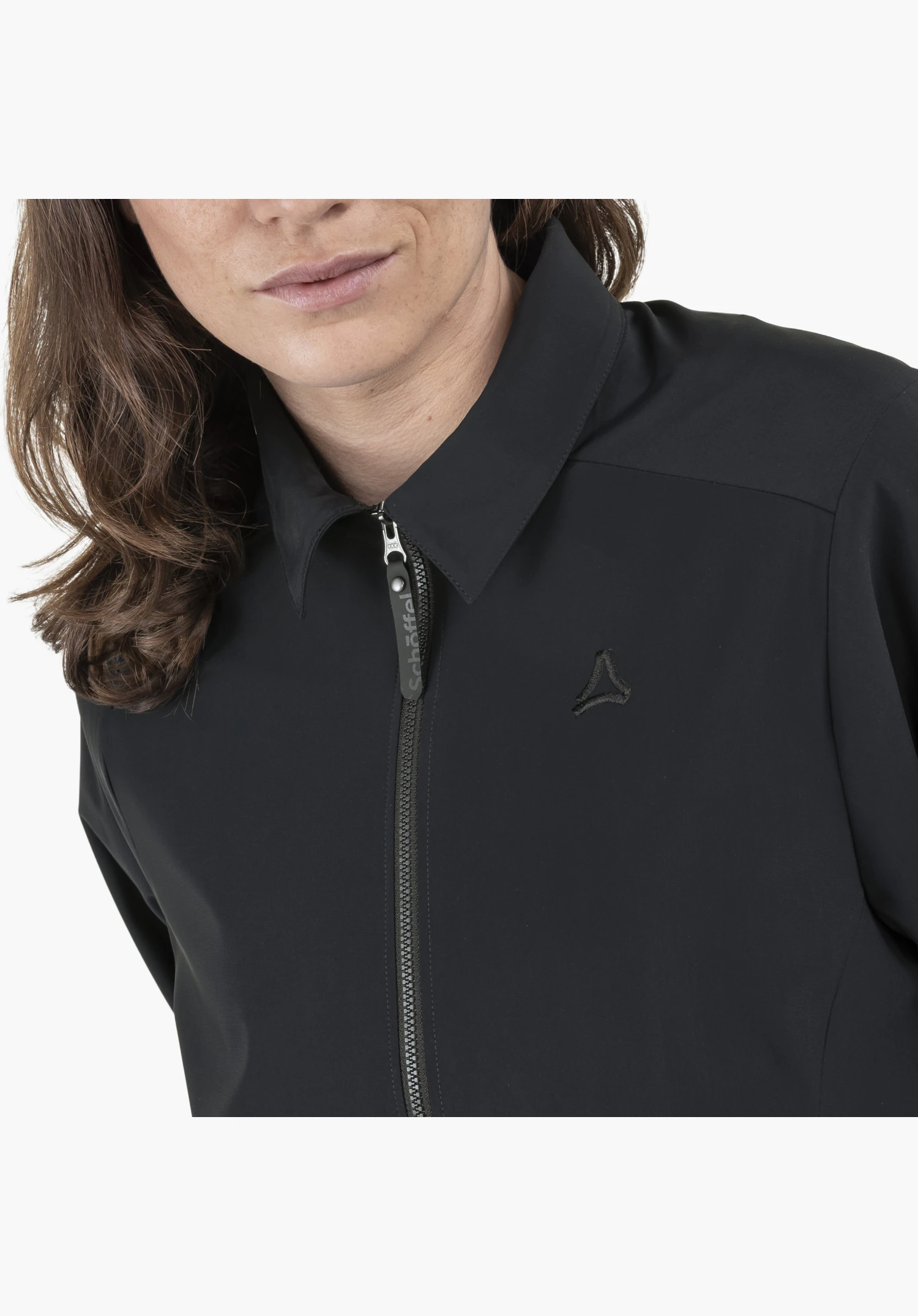 Jersey Jk Style Calmay WMN présente le col, la fermeture éclair frontale avec le lettrage Schöffel sur la tirette et le logo Schöffel discrètement brodé sur le tissu noir lisse, gros plan sur fond blanc/neutre.