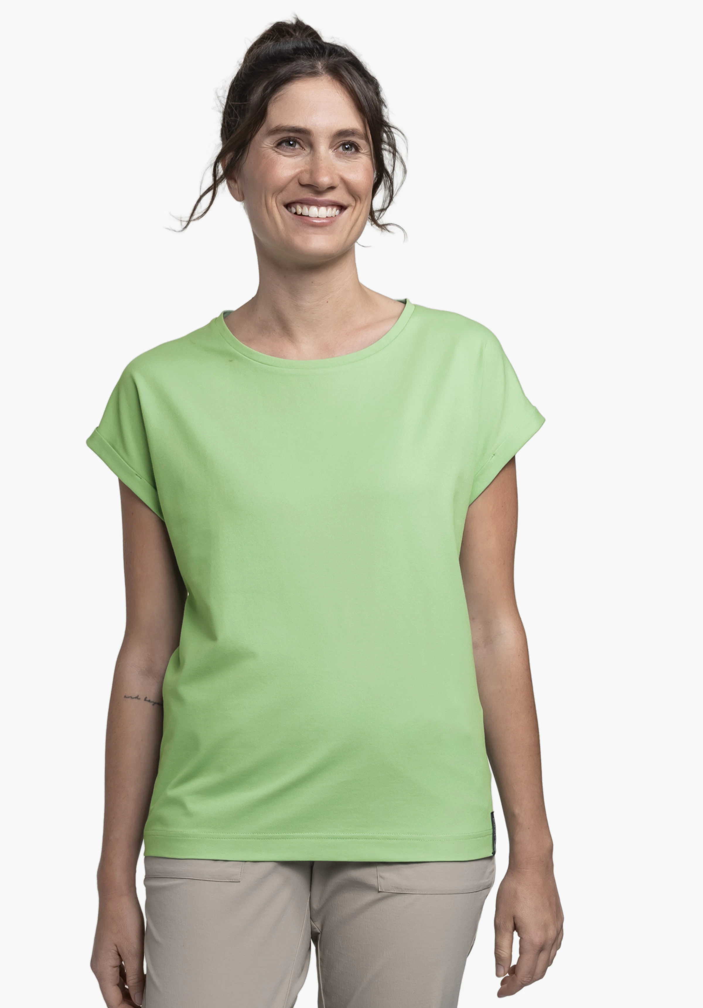 T Shirt Style Serenio WMN in the colour green, worn by a smiling model standing facing forwards, presented against a neutral background.