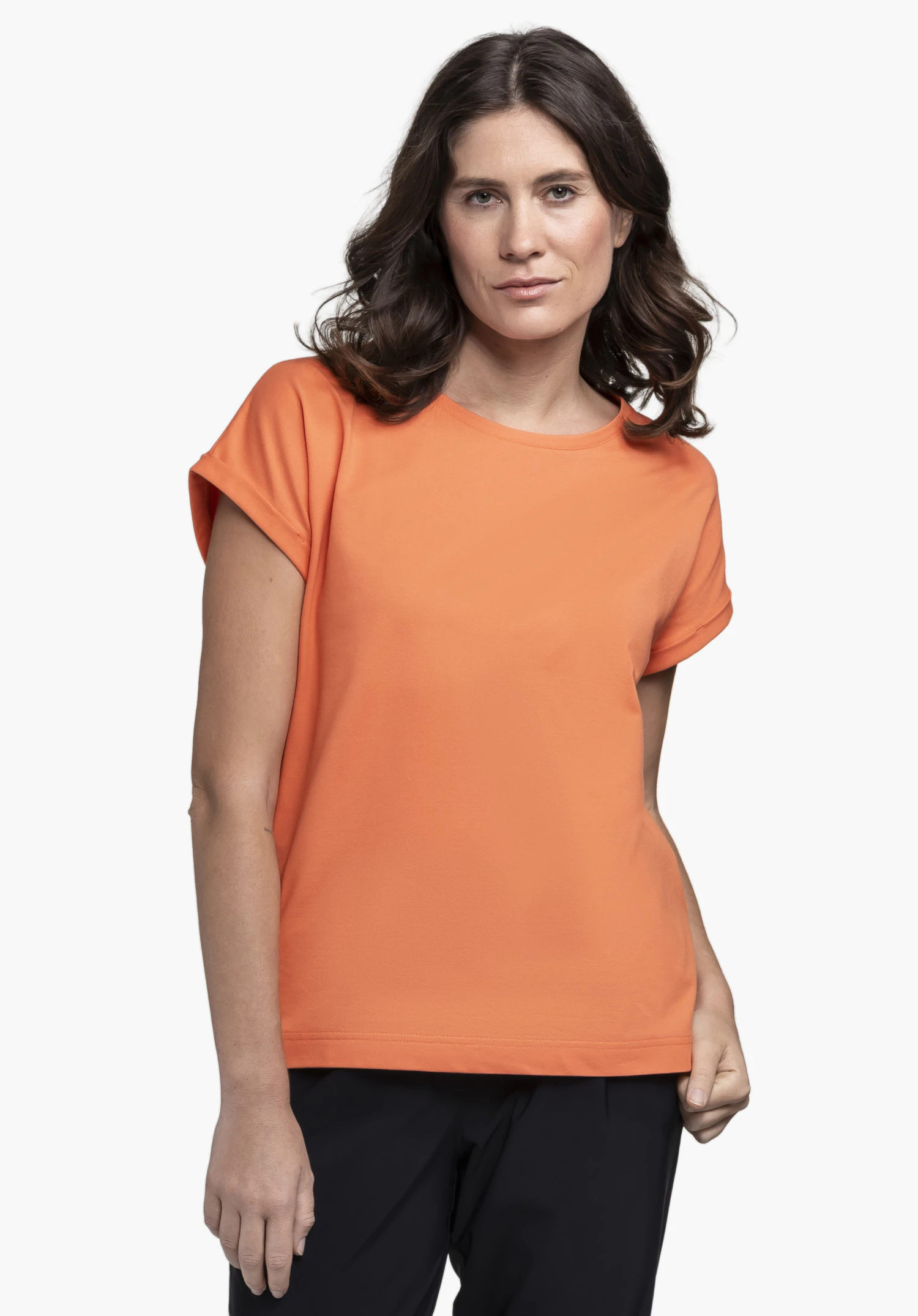 T Shirt Style Serenio WMN in vibrant orange, worn by a model standing front-on against a neutral background. The minimalist T-shirt features a flattering fit, with the subtle Schöffel logo integrated into the overall look.