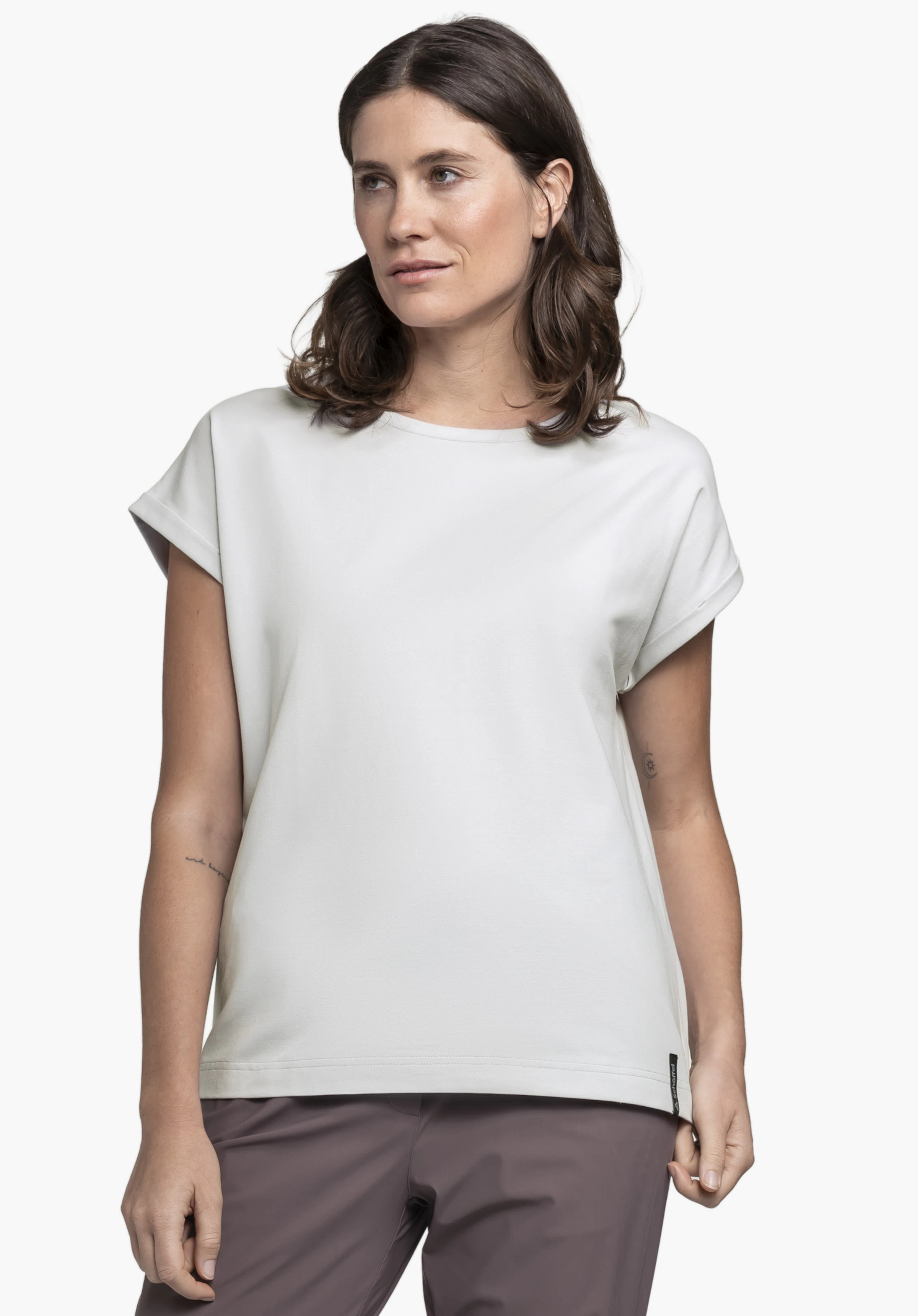 T Shirt Style Serenio WMN en gris porté par un mannequin. Le mannequin se tient de face, regarde sur le côté et porte le t-shirt avec un petit logo Schöffel sur l'ourlet inférieur devant un fond neutre.