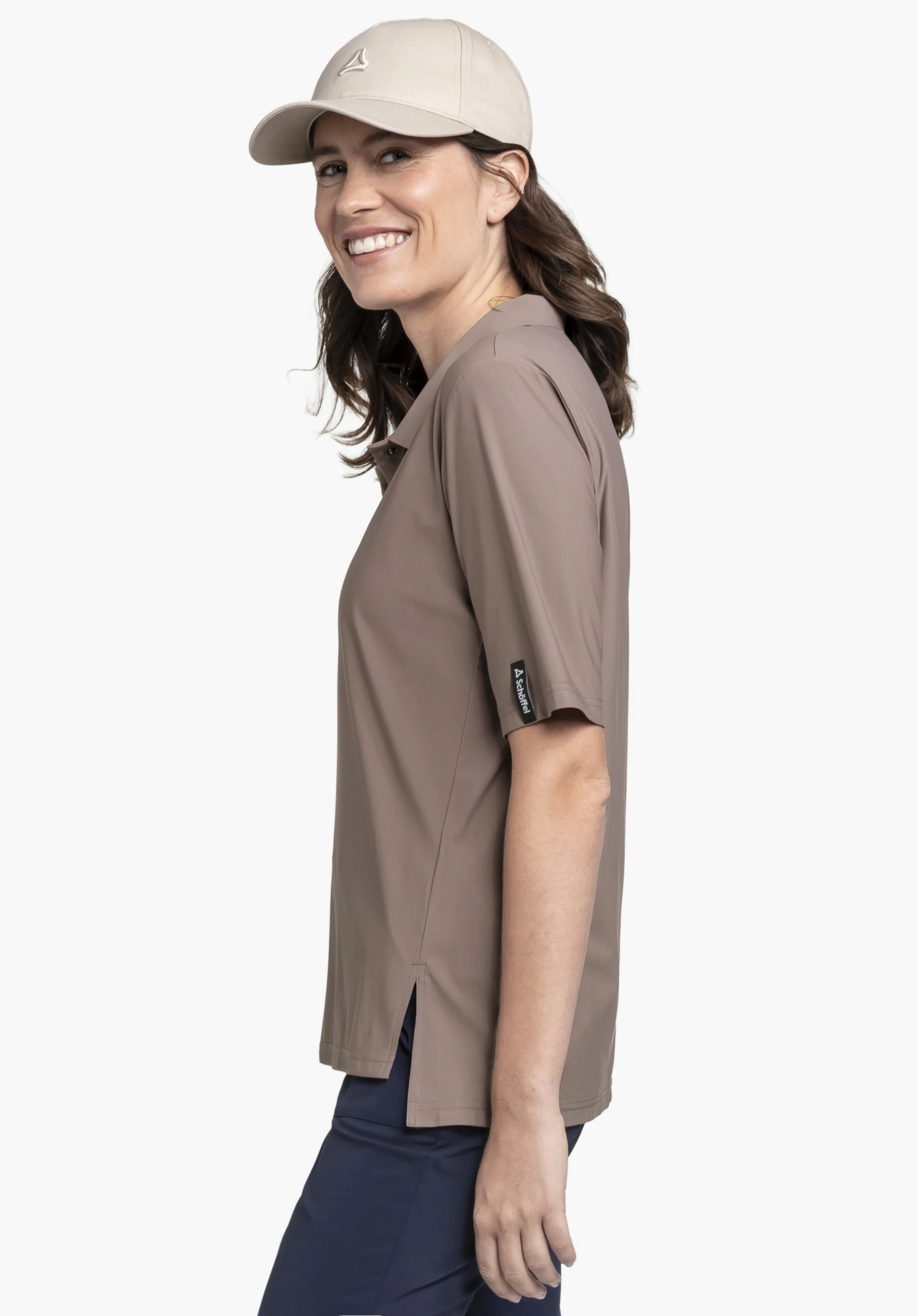 Jersey Polo Style Calmay WMN in brown, worn by a smiling model against a neutral background. The model is standing in profile, highlighting the polo shirt with the subtle Schöffel logo on the sleeve.