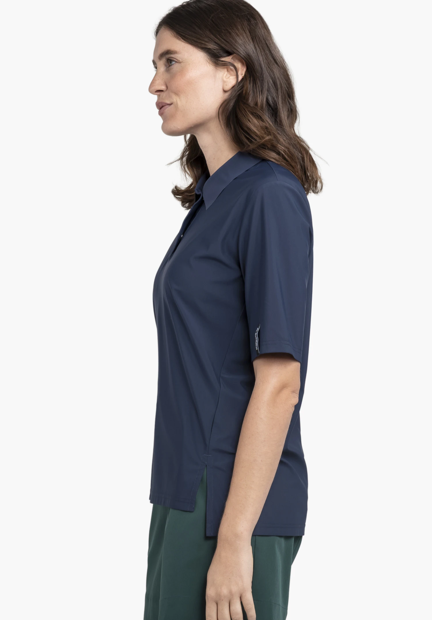 Jersey Polo Style Calmay WMN wird von einem Model getragen, das seitlich steht. Das blaue Poloshirt zeigt ein Schöffel-Logo am Ärmelabschluss und wird vor einem neutralen Hintergrund präsentiert.