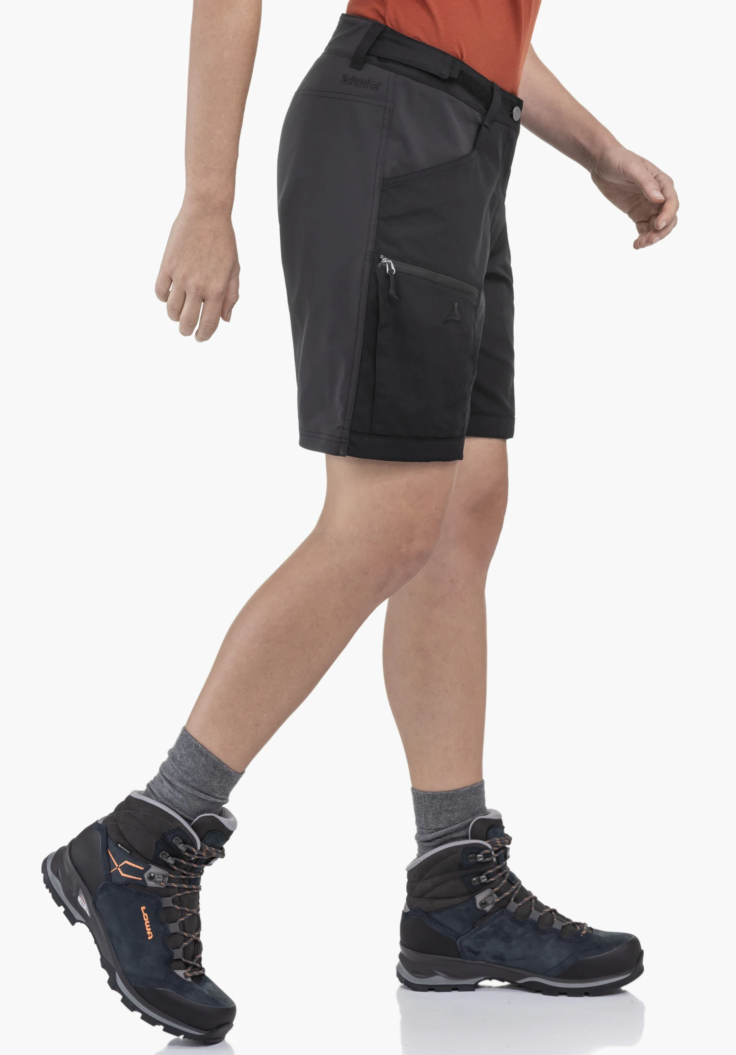 Shorts Style Maghera WMN. On voit un mannequin de profil dans un mouvement de marche, portant le short de couleur noir. Sur un fond neutre, le logo Schöffel au-dessus de la poche de cuisse zippée est bien visible.