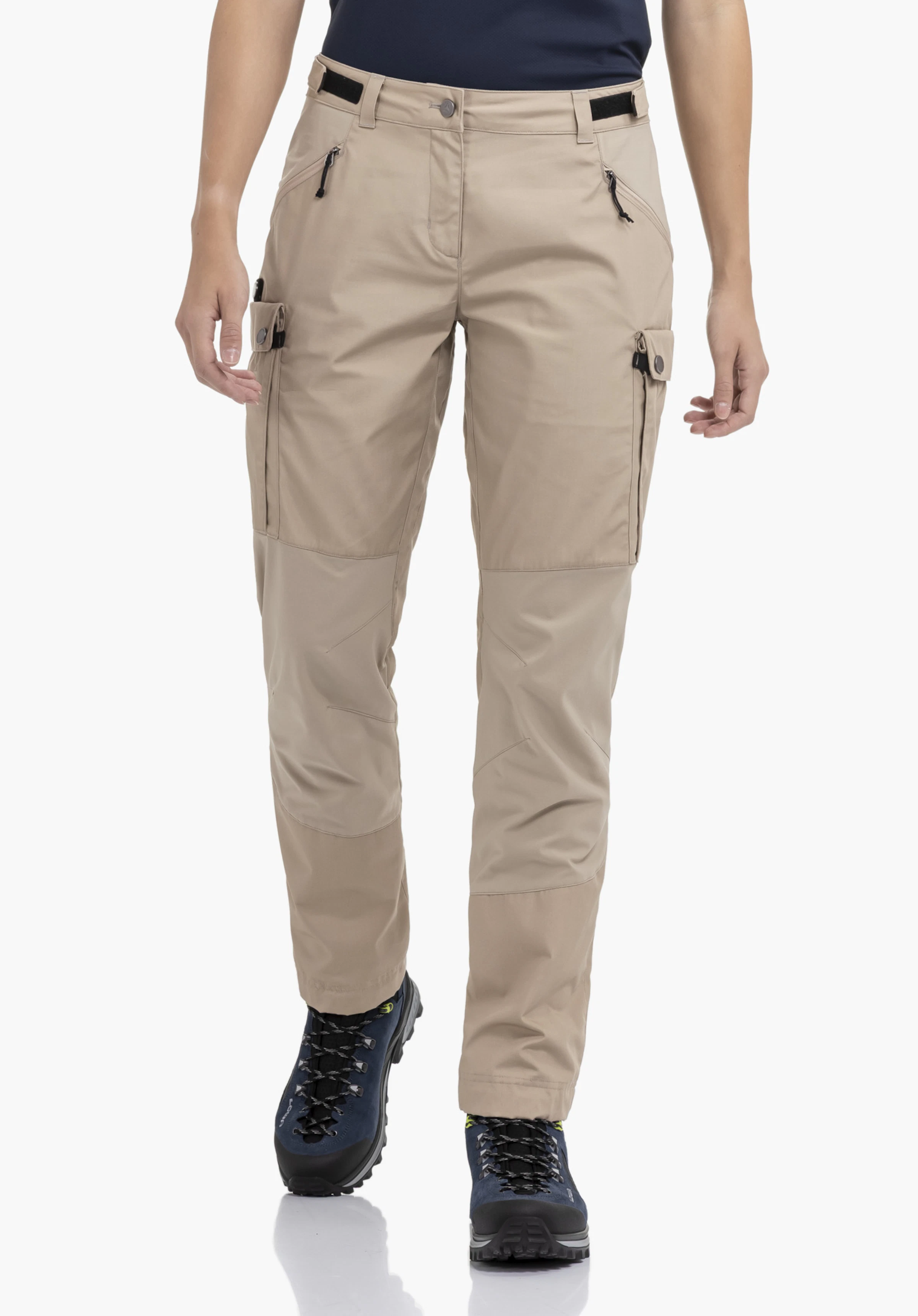 Pants Style Maghera WMN en beige. Le mannequin se tient de face, fait un léger pas en avant et présente le pantalon avec des poches cargo latérales sur un fond neutre.