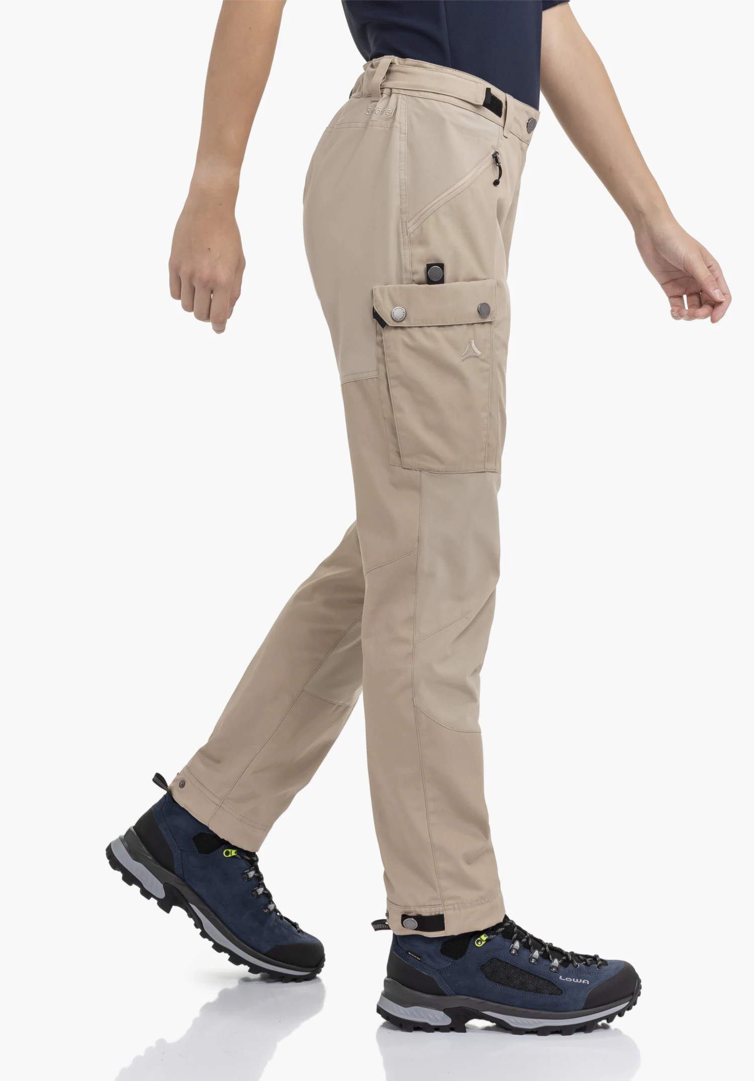 Pants Style Maghera WMN en beige. Le modèle est photographié de profil sur un fond neutre, mettant en valeur le pantalon dans une posture de marche dynamique. Les poches pratiques et le discret logo Schöffel brodé sur la cuisse sont parfaitement visibles.