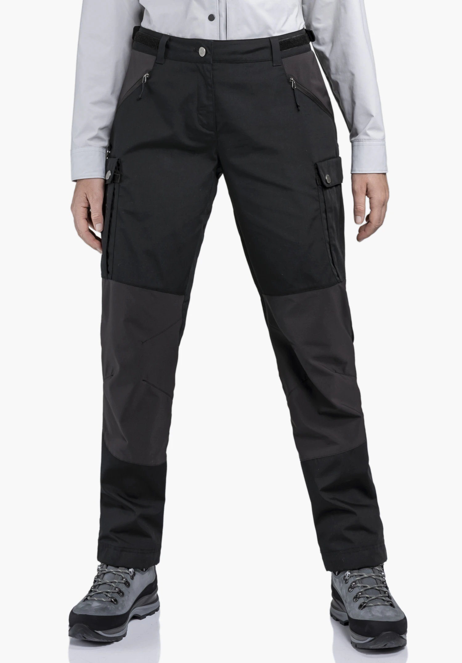 Pants Style Maghera WMN portée par un mannequin se tenant de face. Le pantalon noir présente des poches zippées, des poches cargo sur les cuisses et des empiècements contrastés aux genoux devant un fond neutre.