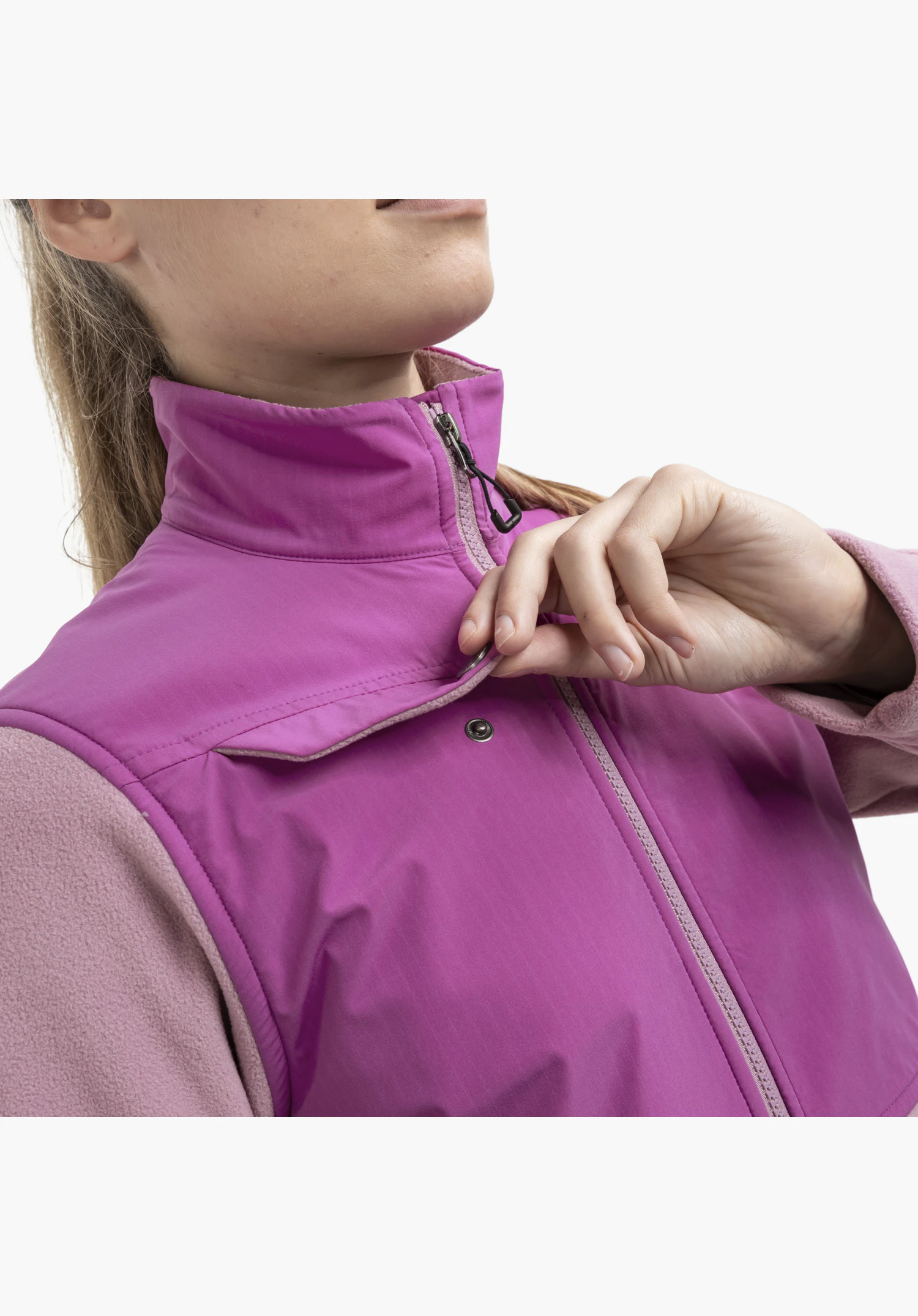 Fleece Jk Style Maghera WMN as a detail shot, where a hand lifts a front fabric flap to reveal a metallic snap fastener next to the main zip, highlighting the contrast between the pink smooth fabric and the fleece. Close-up against a white/neutral background.