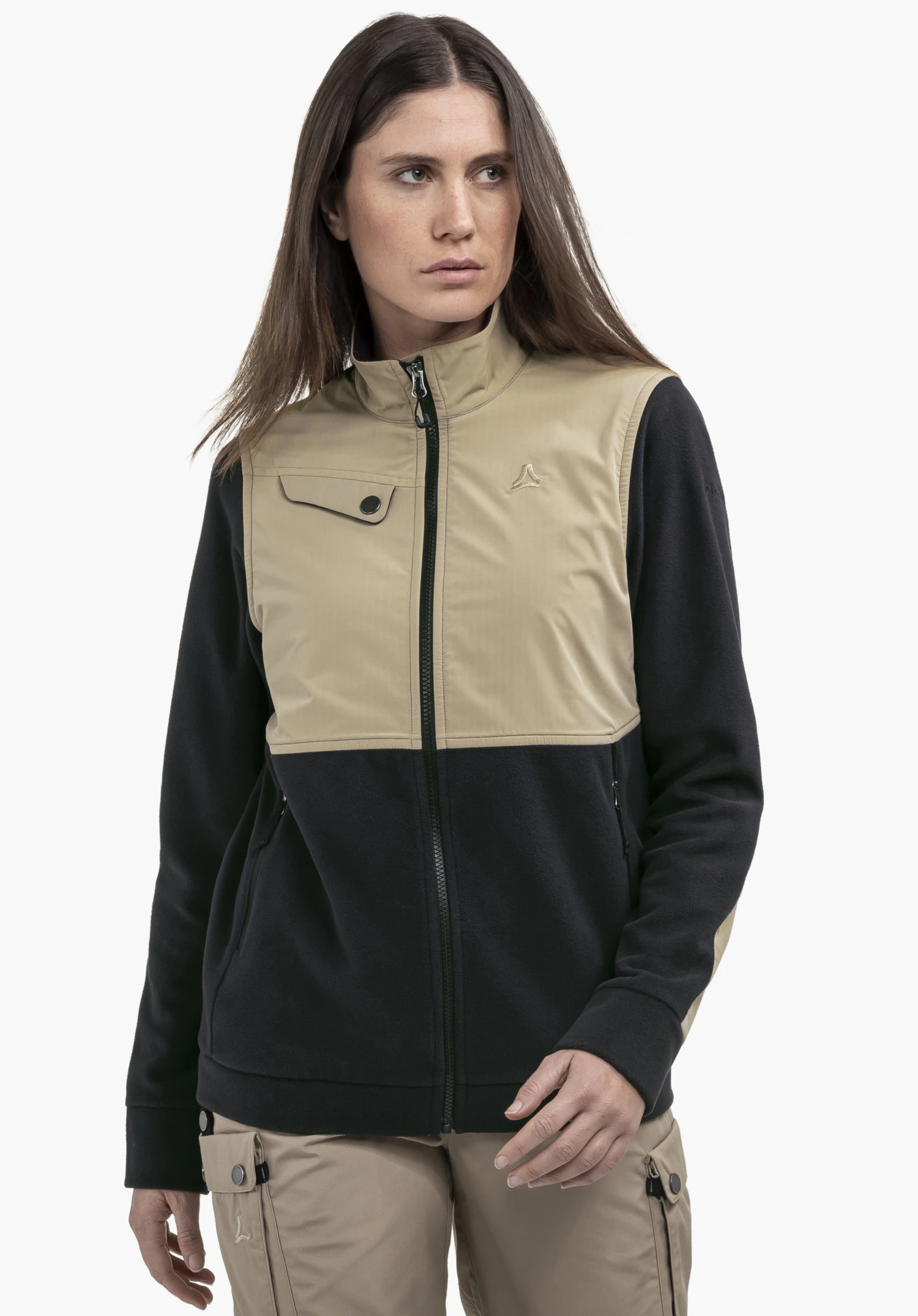 Fleece Jk Style Maghera WMN portée par un mannequin qui se tient de face et regarde sur le côté. La veste polaire présente un design color-block marquant en noir et beige, avec le logo Schöffel visible sur la poitrine gauche, photographiée devant un fond neutre.