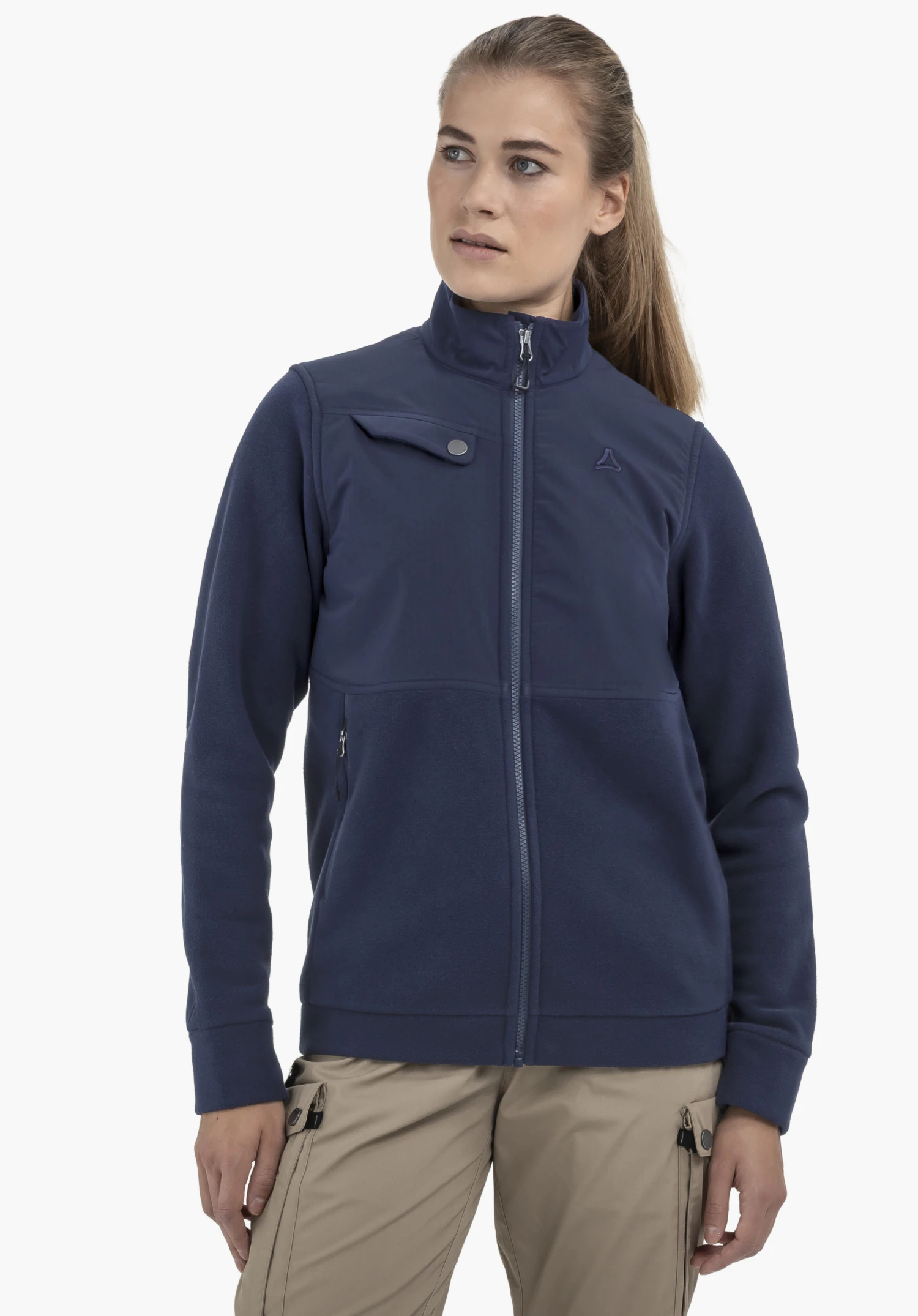 Fleece Jk Style Maghera WMN sur un mannequin de couleur bleue, debout de face et regardant sur le côté. On y voit des détails tels que la fermeture éclair, la poche poitrine et le logo Schöffel sur la poitrine gauche. Le mannequin pose devant un fond neutre.