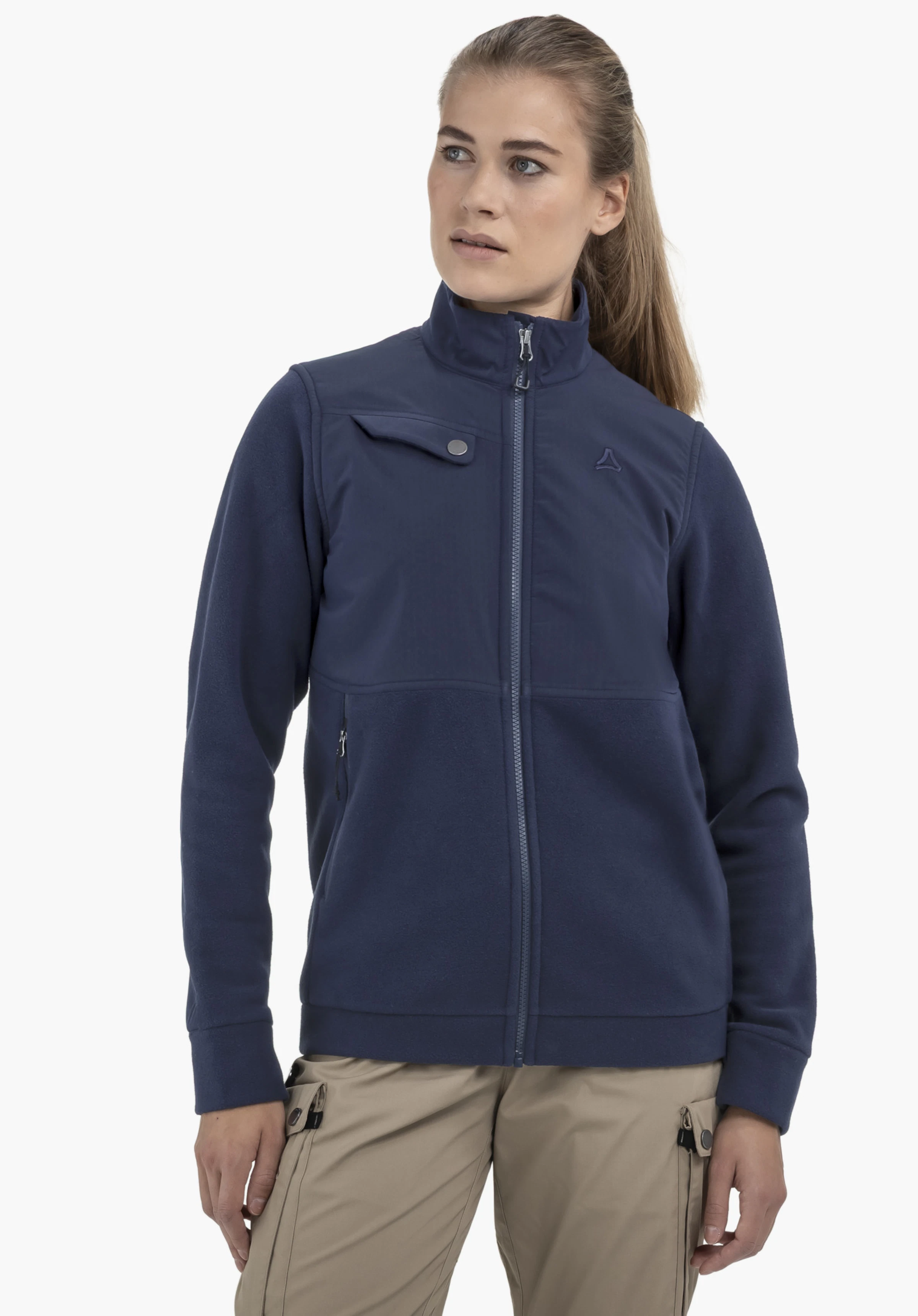 Fleece Jk Style Maghera WMN sur un mannequin de couleur bleue, debout de face et regardant sur le côté. On y voit des détails tels que la fermeture éclair, la poche poitrine et le logo Schöffel sur la poitrine gauche. Le mannequin pose devant un fond neutre.