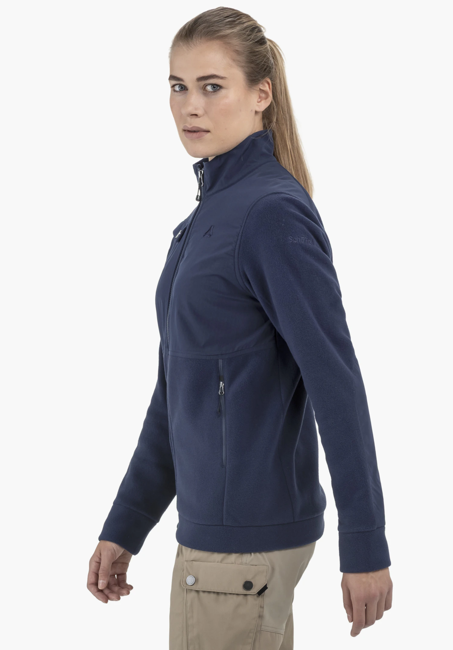 Fleece Jk Style Maghera WMN en bleu : Une femme porte la veste en polaire de profil sur un fond neutre, le logo Schöffel discret étant bien visible sur le haut du bras.