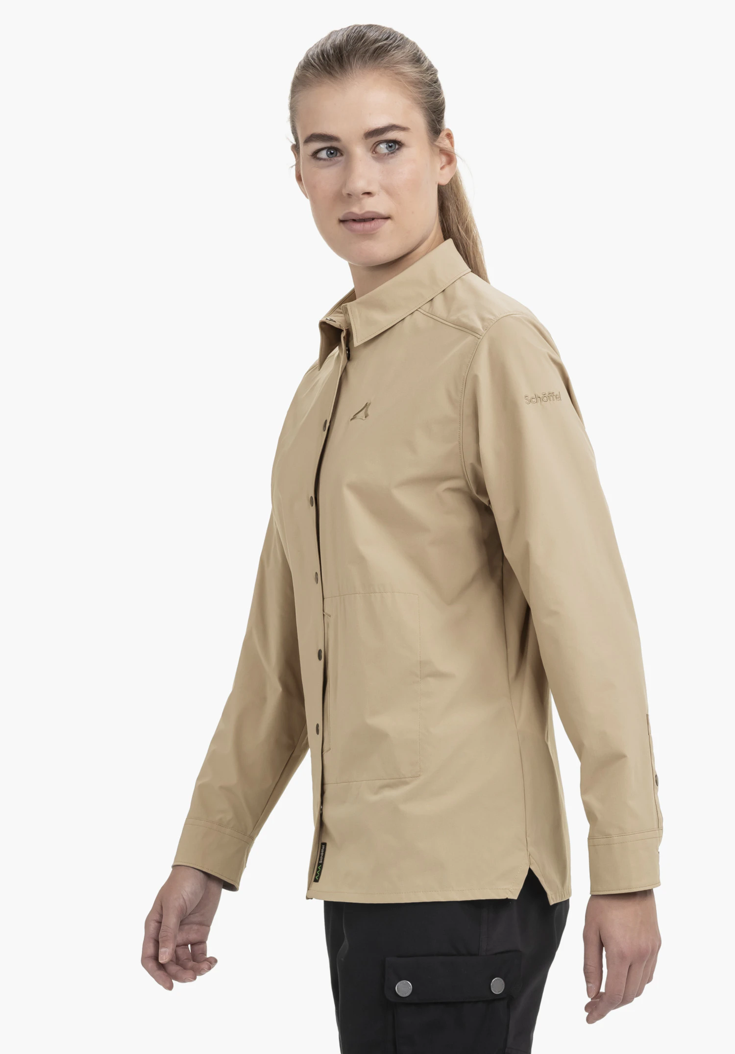 Blouse Style Maghera WMN en beige. La chemise est portée par un mannequin, photographiée de profil sur un fond neutre. L'accent est mis sur la coupe élégante et le discret logo Schöffel sur le haut du bras.