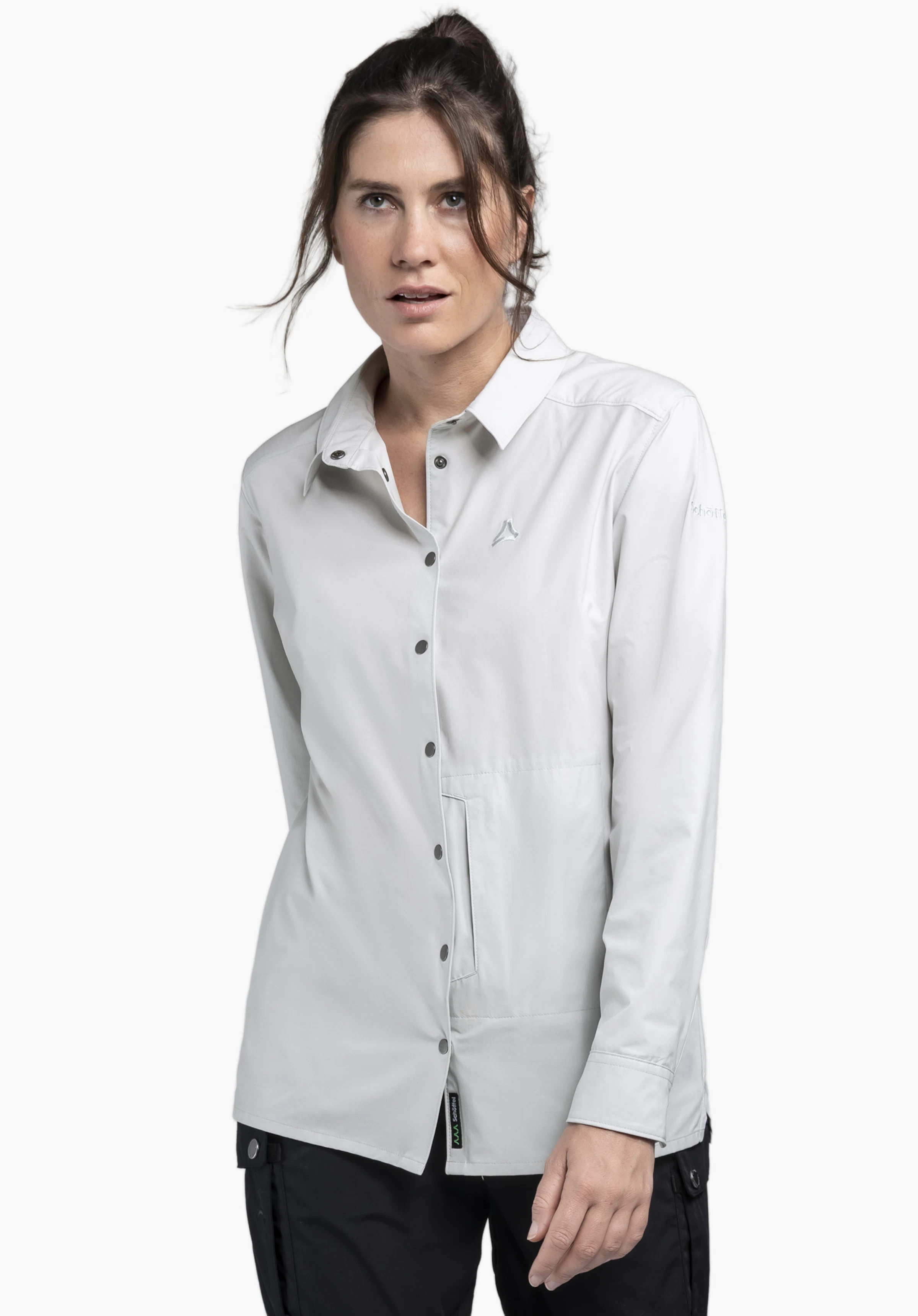 Blouse Style Maghera WMN in Grau präsentiert an einem Model vor neutralem Hintergrund. Die Frau steht frontal zur Kamera und trägt die Bluse mit ihren markanten Druckknöpfen, während das dezente Schöffel-Logo auf der Brust das Design unterstreicht.