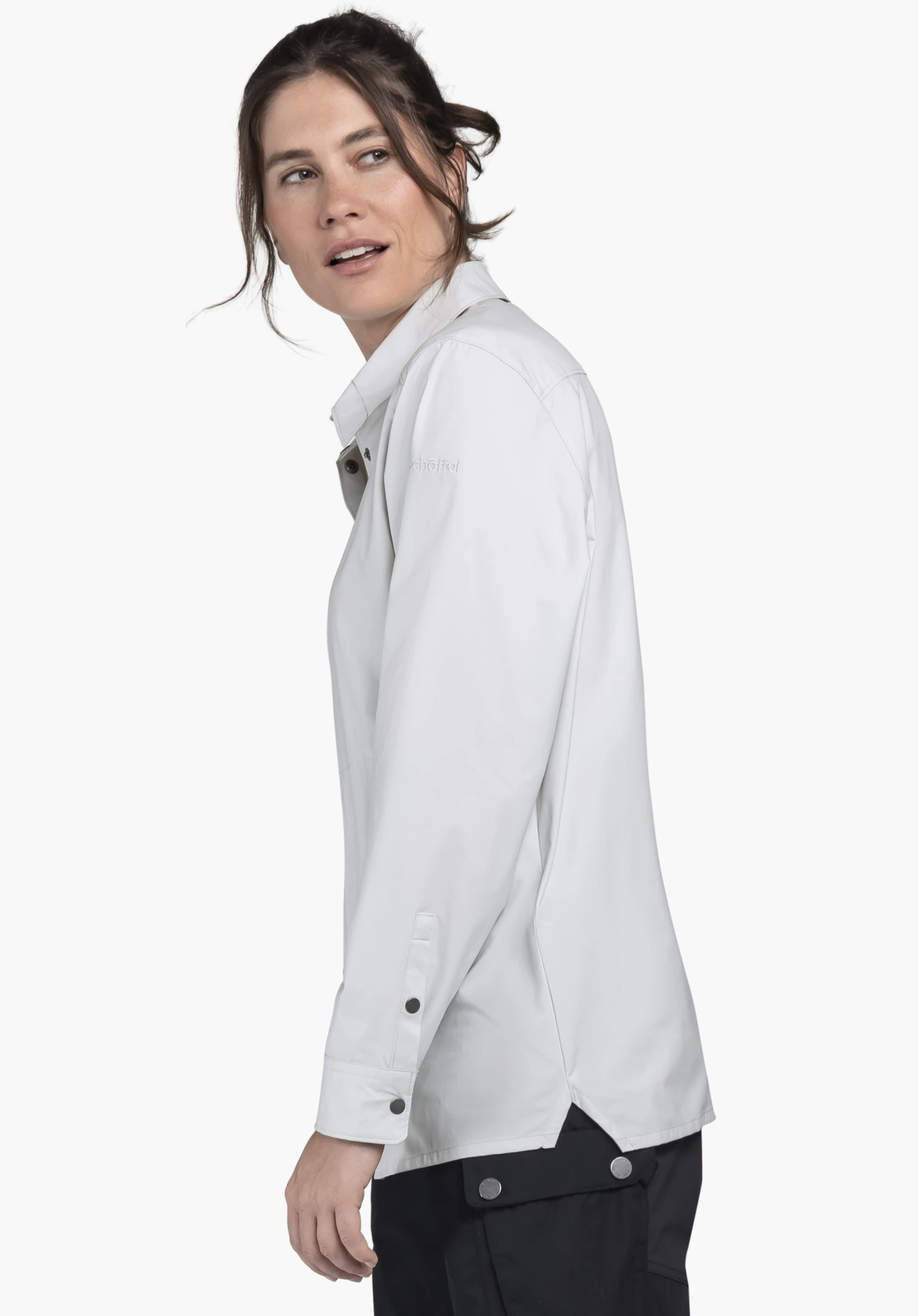 Blouse Style Maghera WMN sur un mannequin se tenant de profil. Le chemisier gris présente le Schöffel-Logo sur le haut du bras et est photographié sur un fond neutre.