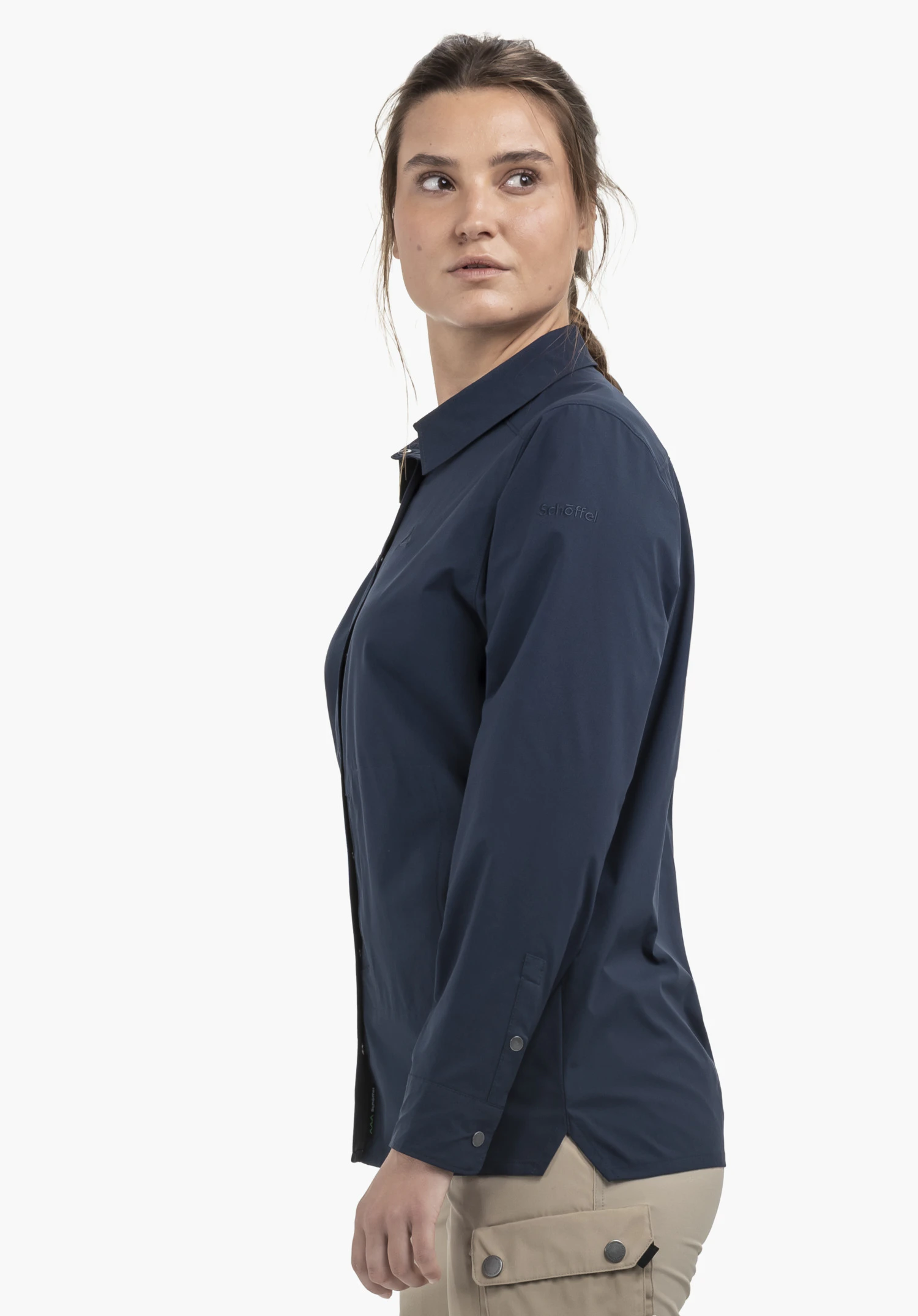 Blouse Style Maghera WMN in Blau präsentiert von einem Model, das seitlich in die Kamera blickt. Die Bluse zeigt vor einem neutralen Hintergrund das dezente Schöffel-Logo am Oberarm.