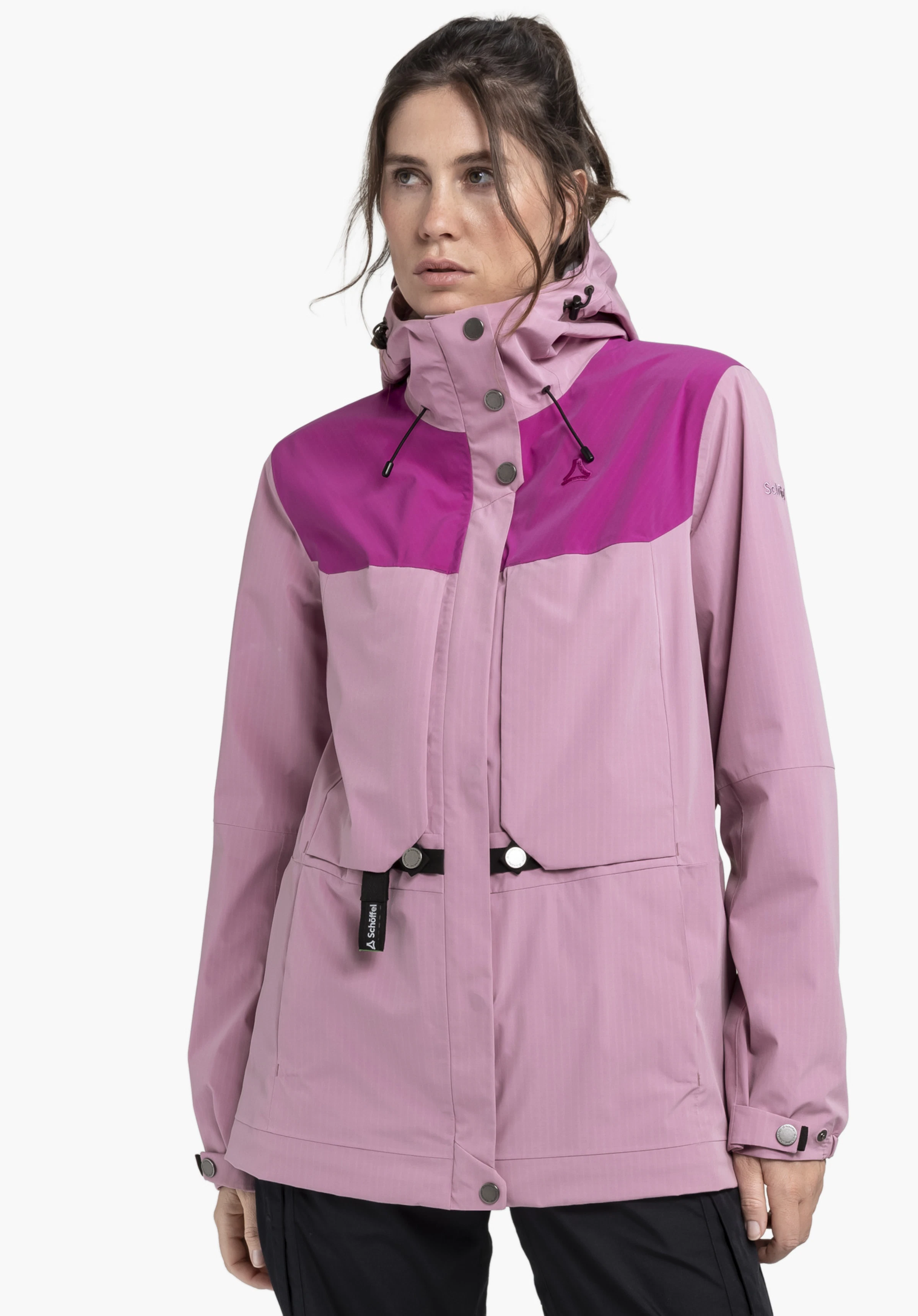2L Jacket Style Maghera WMN in einem sanften Rosa vor neutralem Hintergrund. Das Model ist frontal abgebildet und präsentiert die hochwertige Funktionsjacke, deren Design durch kontrastierende Details akzentuiert wird. Das dezente Schöffel-Logo ist im Brustbereich und am Ärmel erkennbar.