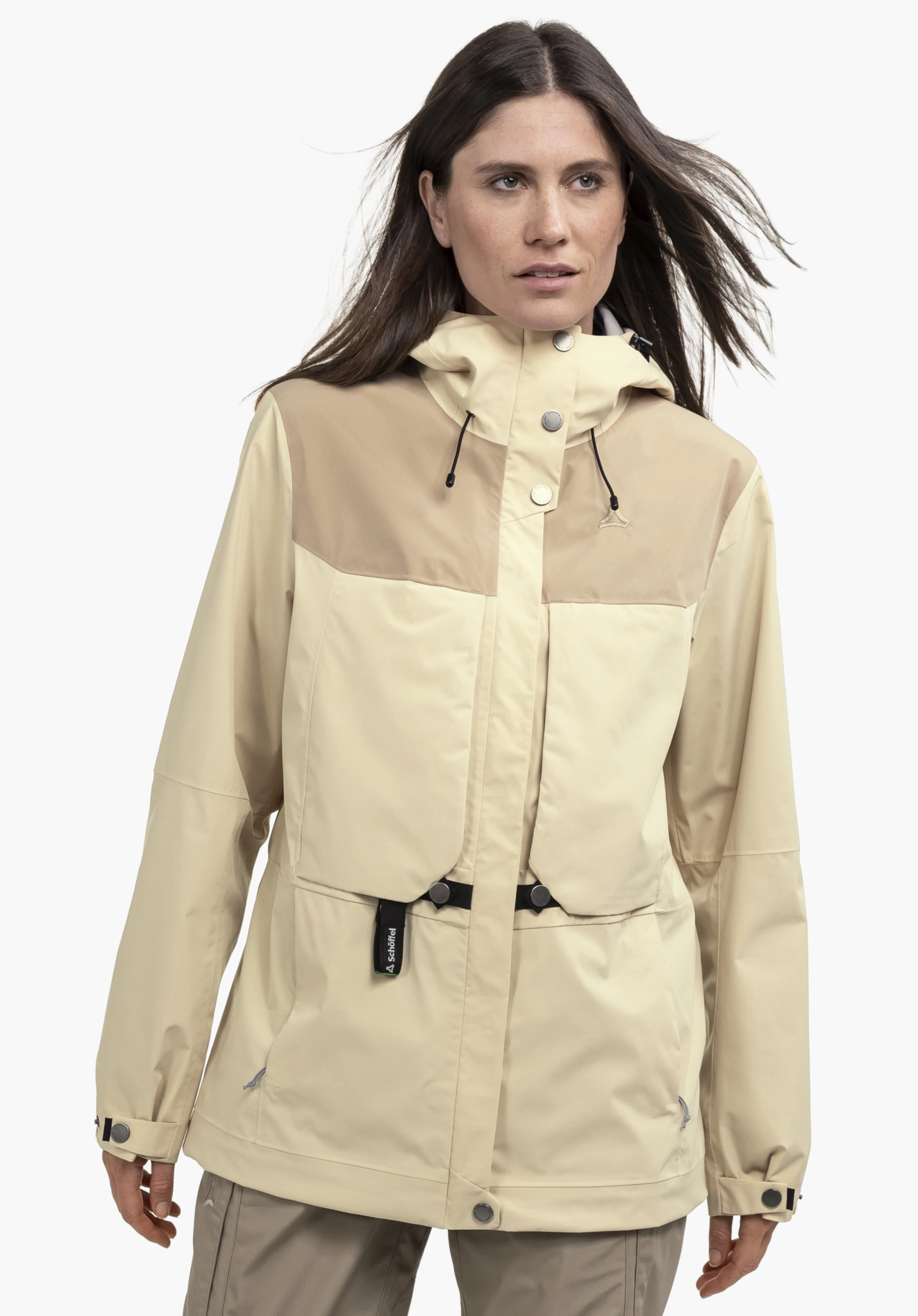 2L Jacket Style Maghera WMN in beige. The front view shows a model posing in front of a neutral background, highlighting the jacket's functional hood. The subtle Schöffel logo is clearly visible.