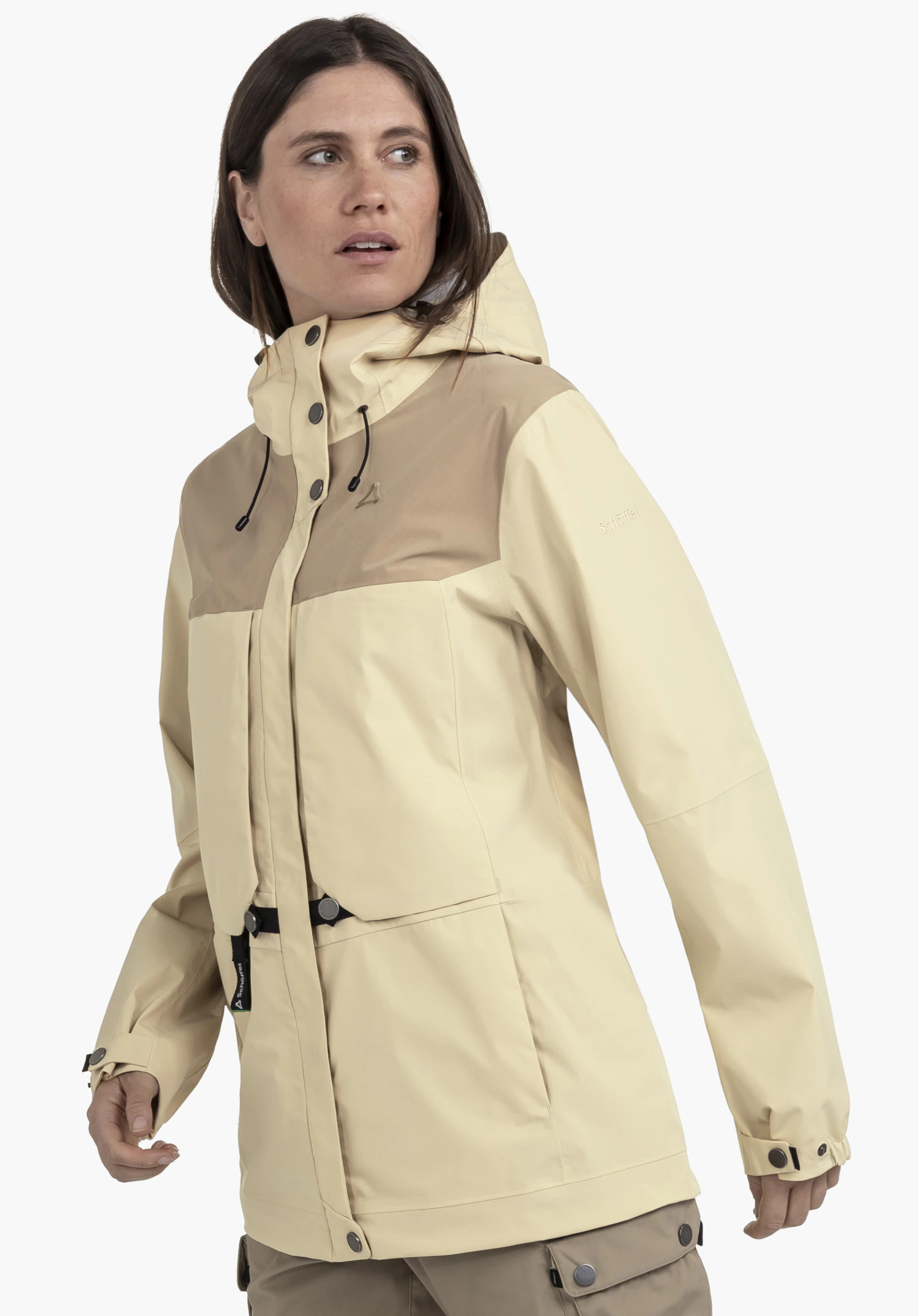2L Jacket Style Maghera WMN worn by a model standing slightly sideways and looking to the side. The beige jacket features darker panels on the chest area alongside a visible Schöffel logo on the chest and sleeve, set against a neutral background.