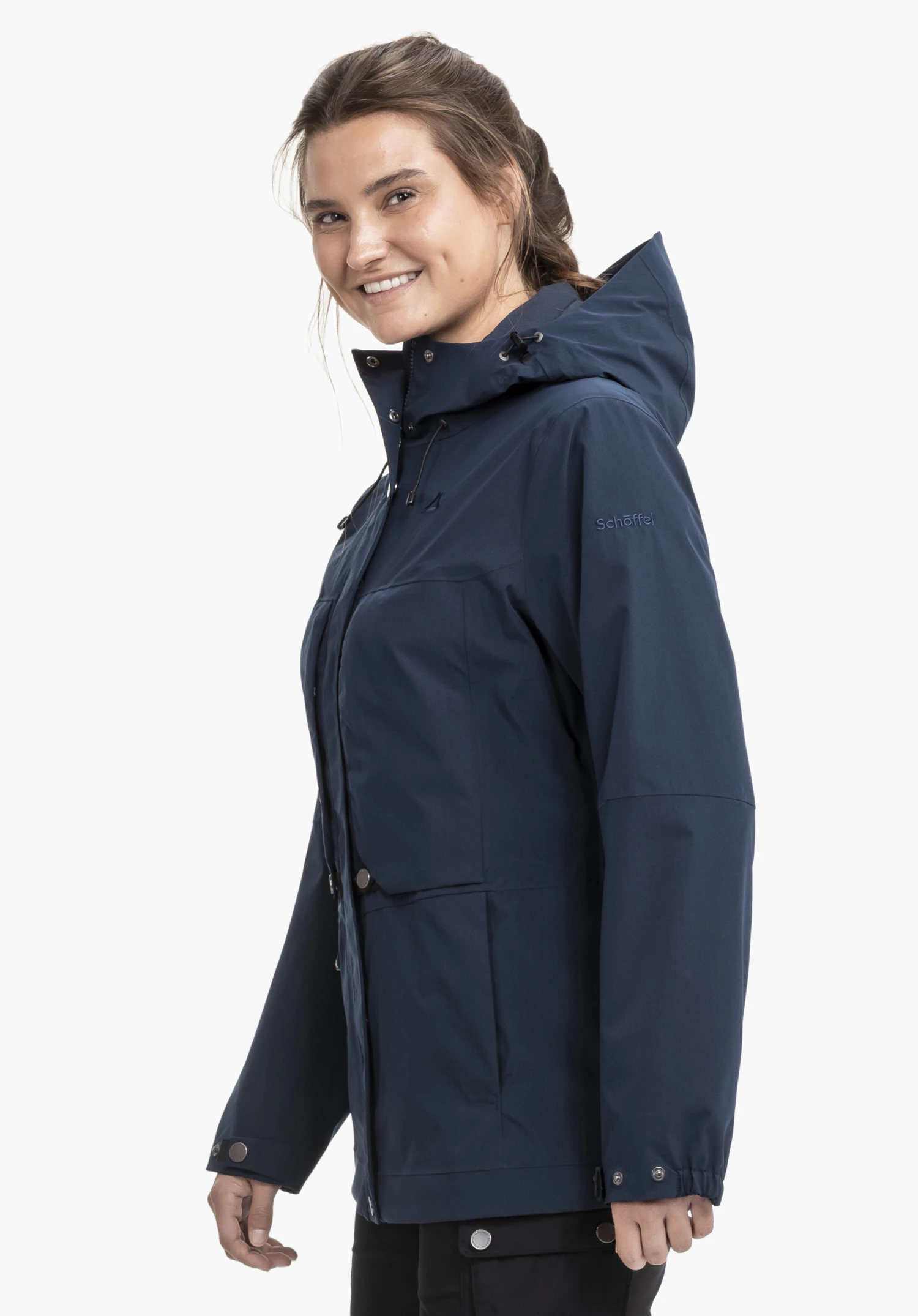 2L Jacket Style Maghera WMN portée par un mannequin souriant qui se tient de profil. La veste bleue présente le logo Schöffel sur la manche gauche et est présentée sur un fond neutre.