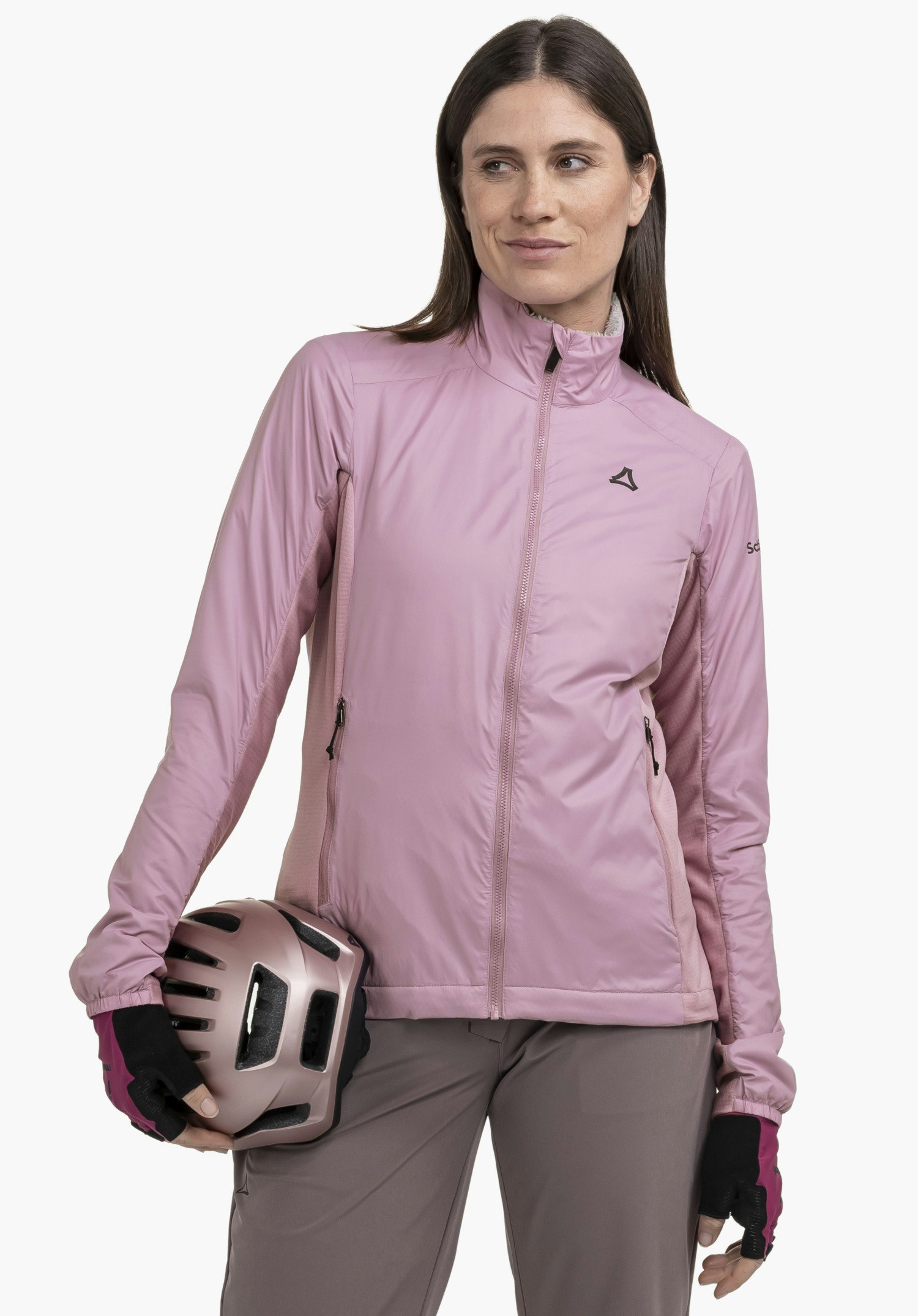 Ins Jacket Style Samaia WMN. A model stands frontally in front of a neutral background, wearing the pink jacket with a visible Schöffel-Logo on the chest whilst holding a cycling helmet in her hand.