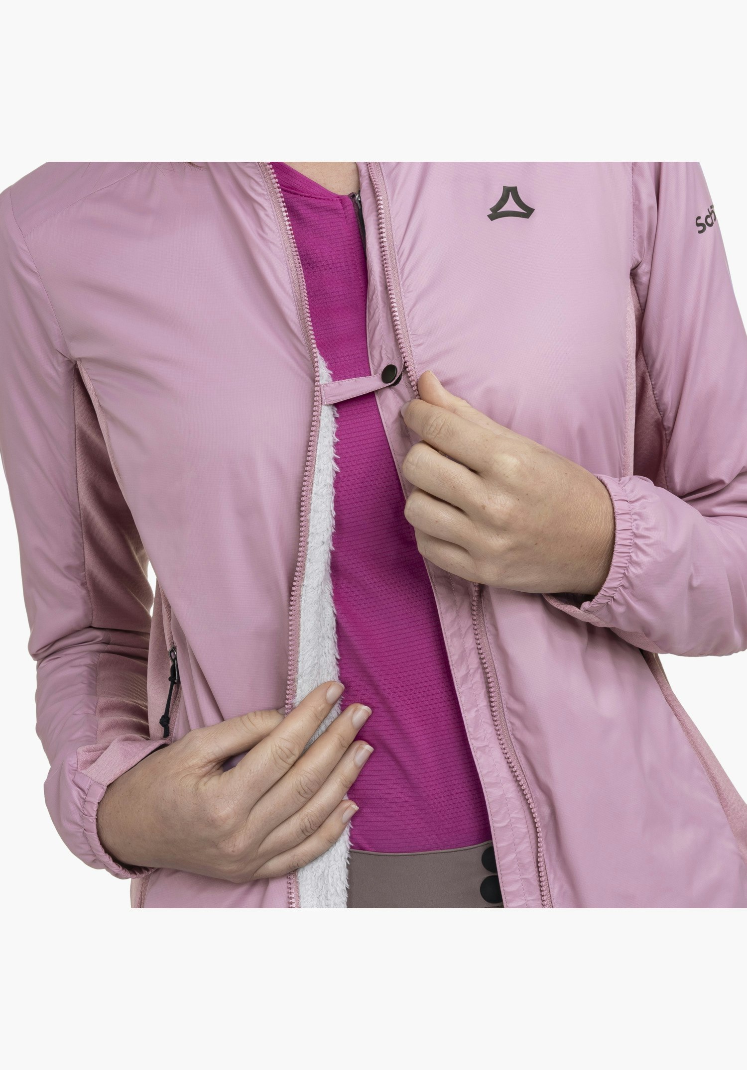 Ins Jacket Style Samaia WMN in Rosa mit Fokus auf den geöffneten Frontreißverschluss, der das flauschige weiße Innenfutter freilegt. Ein schmaler Riegel mit Druckknopf verbindet die Kanten, und das Schöffel-Logo ist deutlich auf der Brust platziert als Nahaufnahme vor weißem Hintergrund.