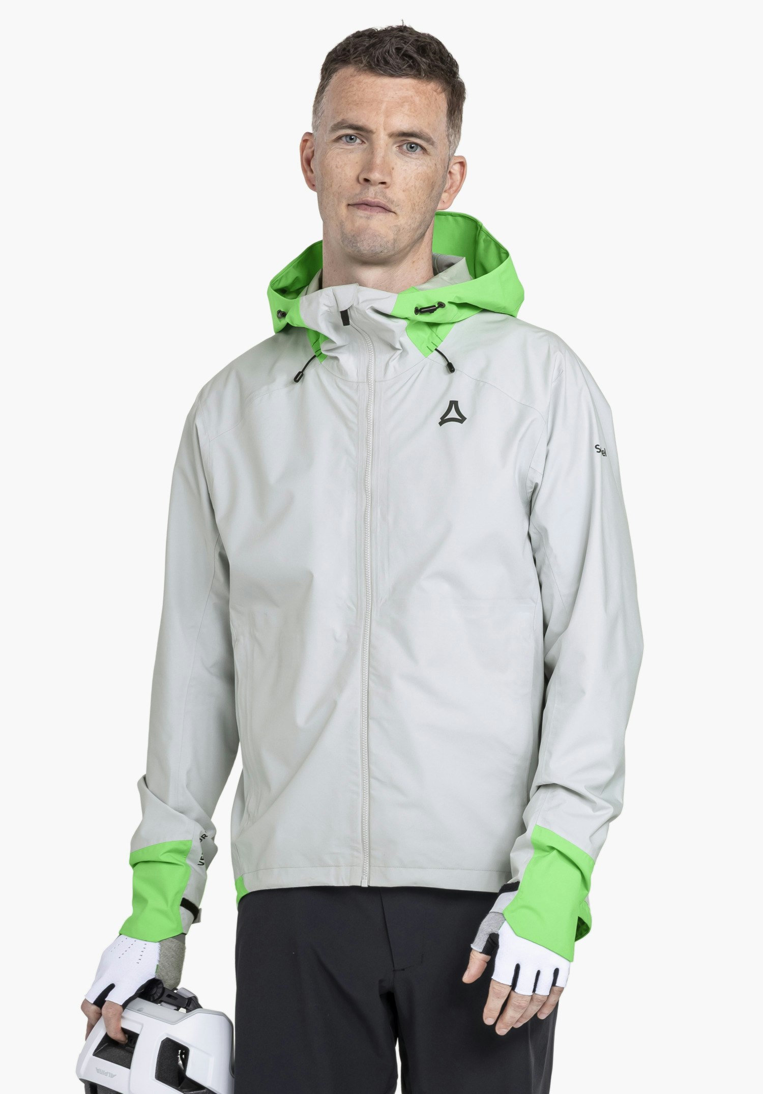 2.5L Jacket Style Tajiva MEN: A model stands frontally against a neutral background wearing the jacket in the colour grey. The Schöffel-Logo is visible on the left chest, while the man holds a cycling helmet in his hand.