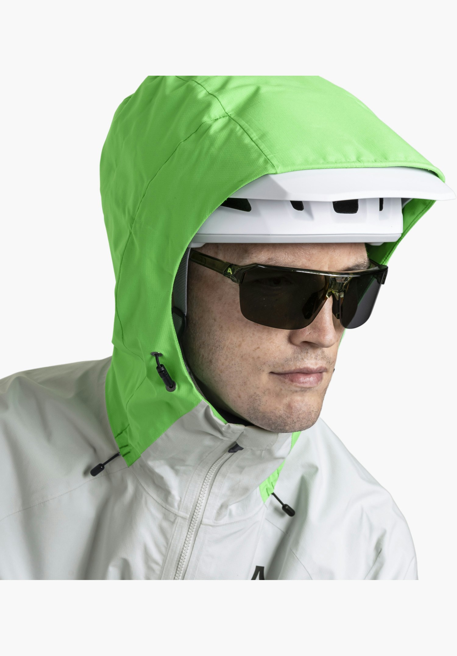 2.5L Jacket Style Tajiva MEN shows the grey fabric, the front zip, the black toggles of the green hood and a partial Schöffel logo at the bottom edge, worn over a cycling helmet. Close-up against a white background.