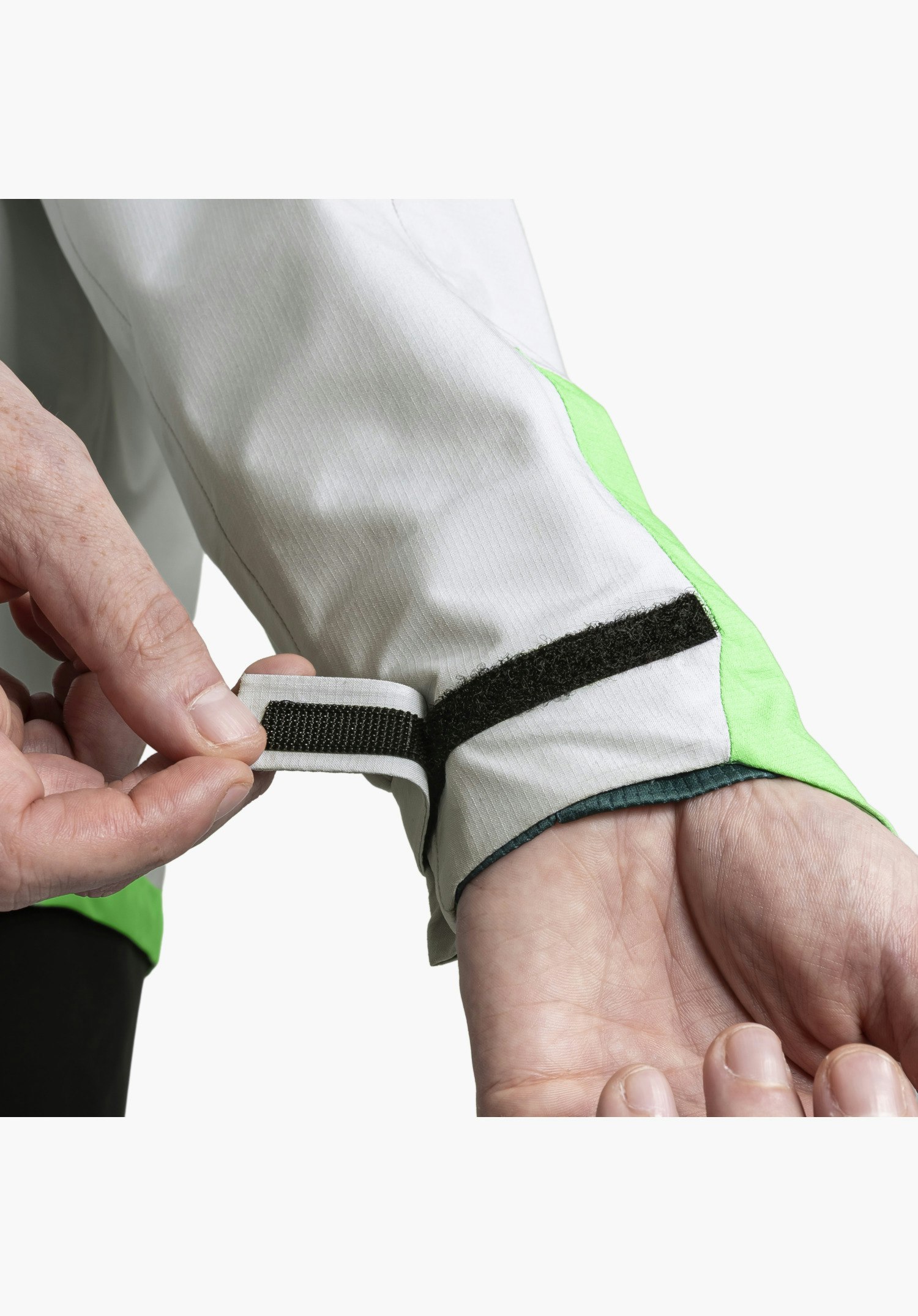 2.5L Jacket Style Tajiva MEN shows the adjustable hook-and-loop fastener on the sleeve cuff of the grey fabric, which is currently being adjusted by two hands for an optimal fit. Close-up against a white/neutral background.