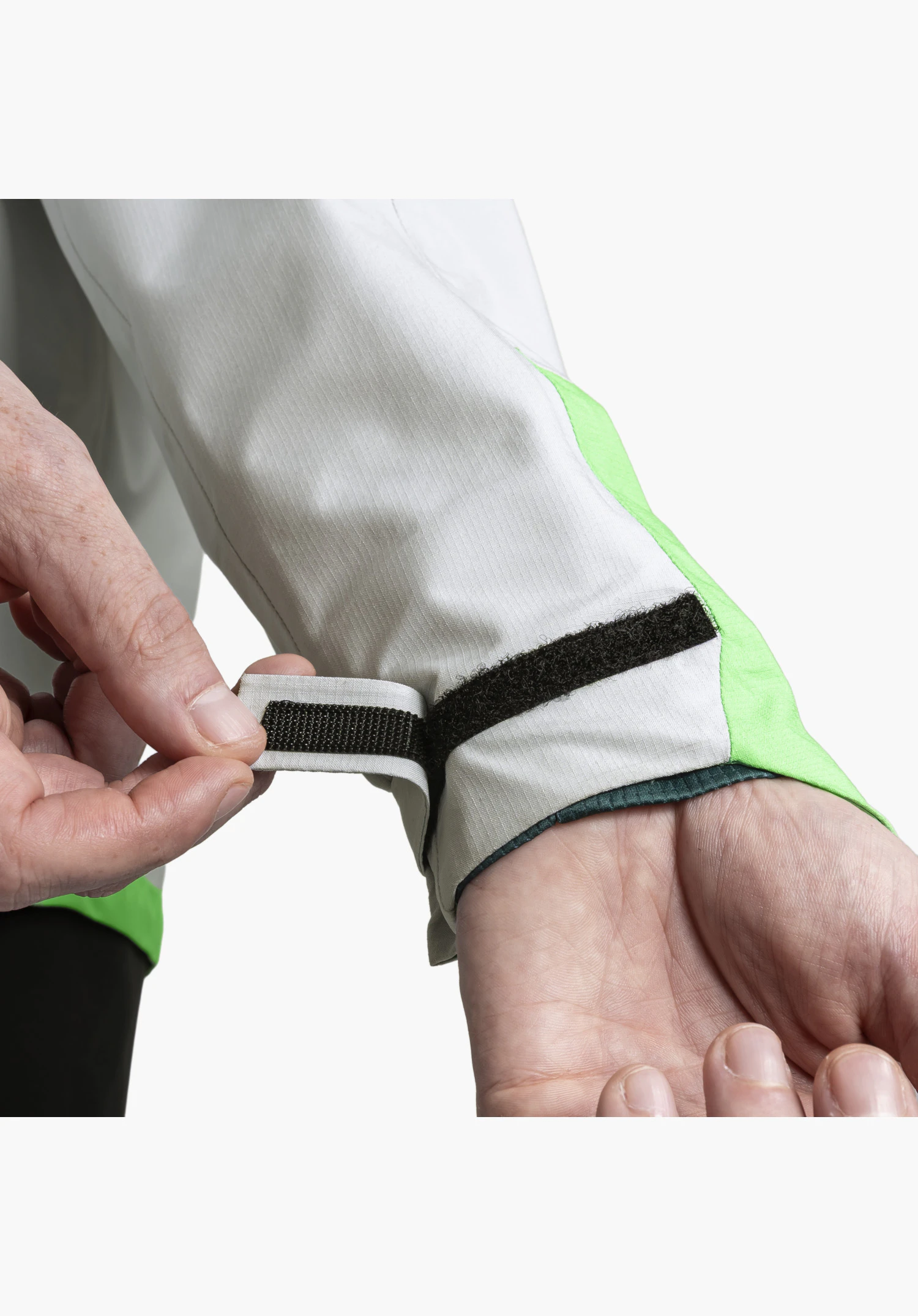 2.5L Jacket Style Tajiva MEN shows the adjustable hook-and-loop fastener on the sleeve cuff of the grey fabric, which is currently being adjusted by two hands for an optimal fit. Close-up against a white/neutral background.