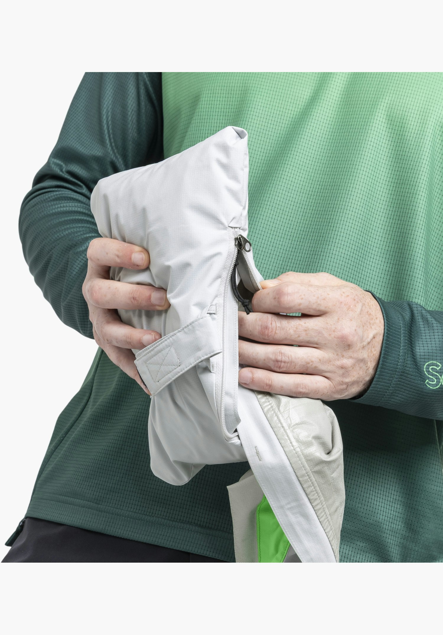 2.5L Jacket Style Tajiva MEN, detail of the grey fabric structure and the zip of the integrated pack-away pocket while stowing the material, close-up against a white/neutral background.