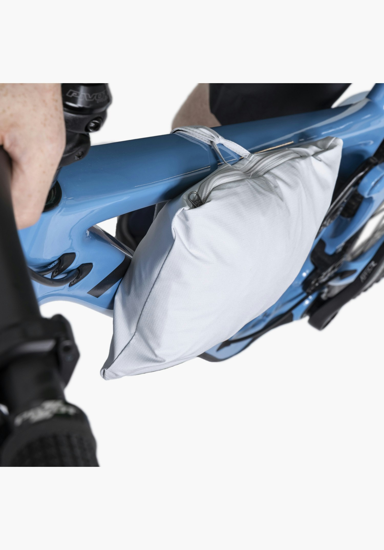 2.5L Jacket Style Tajiva MEN in grey, practically packed away in its own pocket and attached to the frame of a blue mountain bike, while one hand of the rider grips the handlebar.