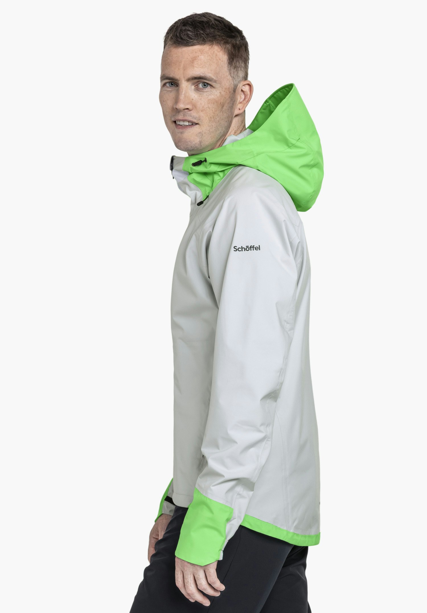 2.5L Jacket Style Tajiva MEN: A model wearing the grey jacket is captured in a side profile pose, looking towards the camera. The subtle Schöffel logo on the upper arm is clearly visible against the neutral background.