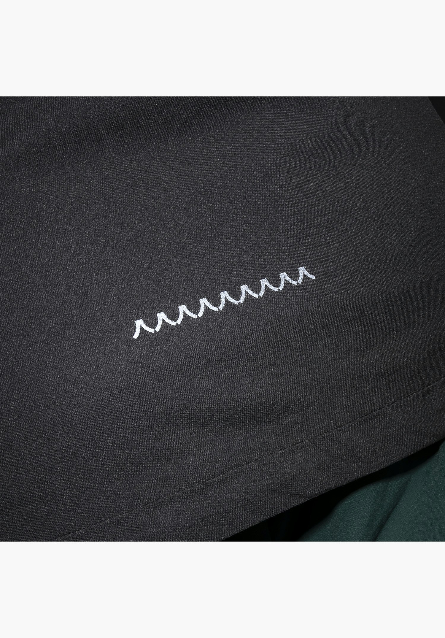 2.5L Jacket Style Tajiva MEN, Detail des weißen Schöffel-Logos auf dem schwarzen Stoff, Nahaufnahme vor weißem/neutralem Hintergrund.