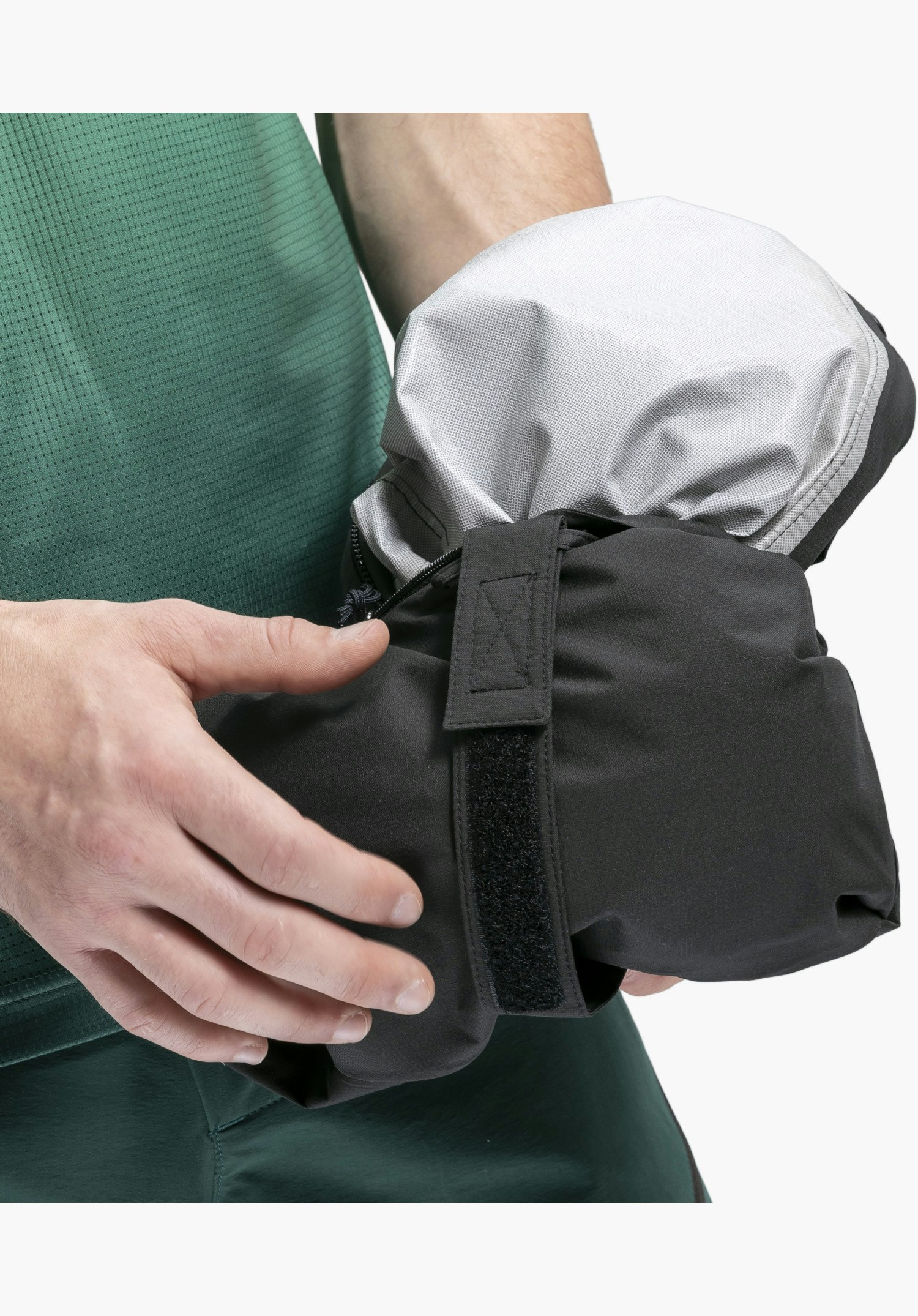 2.5L Jacket Style Tajiva MEN, Detail des schwarzen Außenmaterials mit Klettverschluss-Riemen und silbernem Innenfutter, zusammengefaltet in den Händen einer Person. Nahaufnahme vor weißem/neutralem Hintergrund.