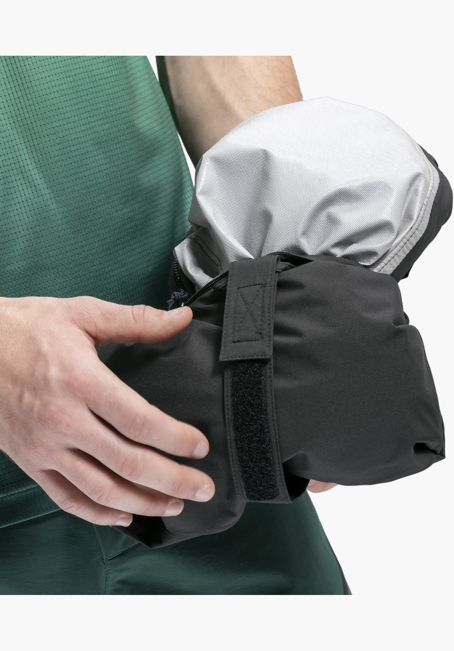 2.5L Jacket Style Tajiva MEN, Detail des schwarzen Außenmaterials mit Klettverschluss-Riemen und silbernem Innenfutter, zusammengefaltet in den Händen einer Person. Nahaufnahme vor weißem/neutralem Hintergrund.