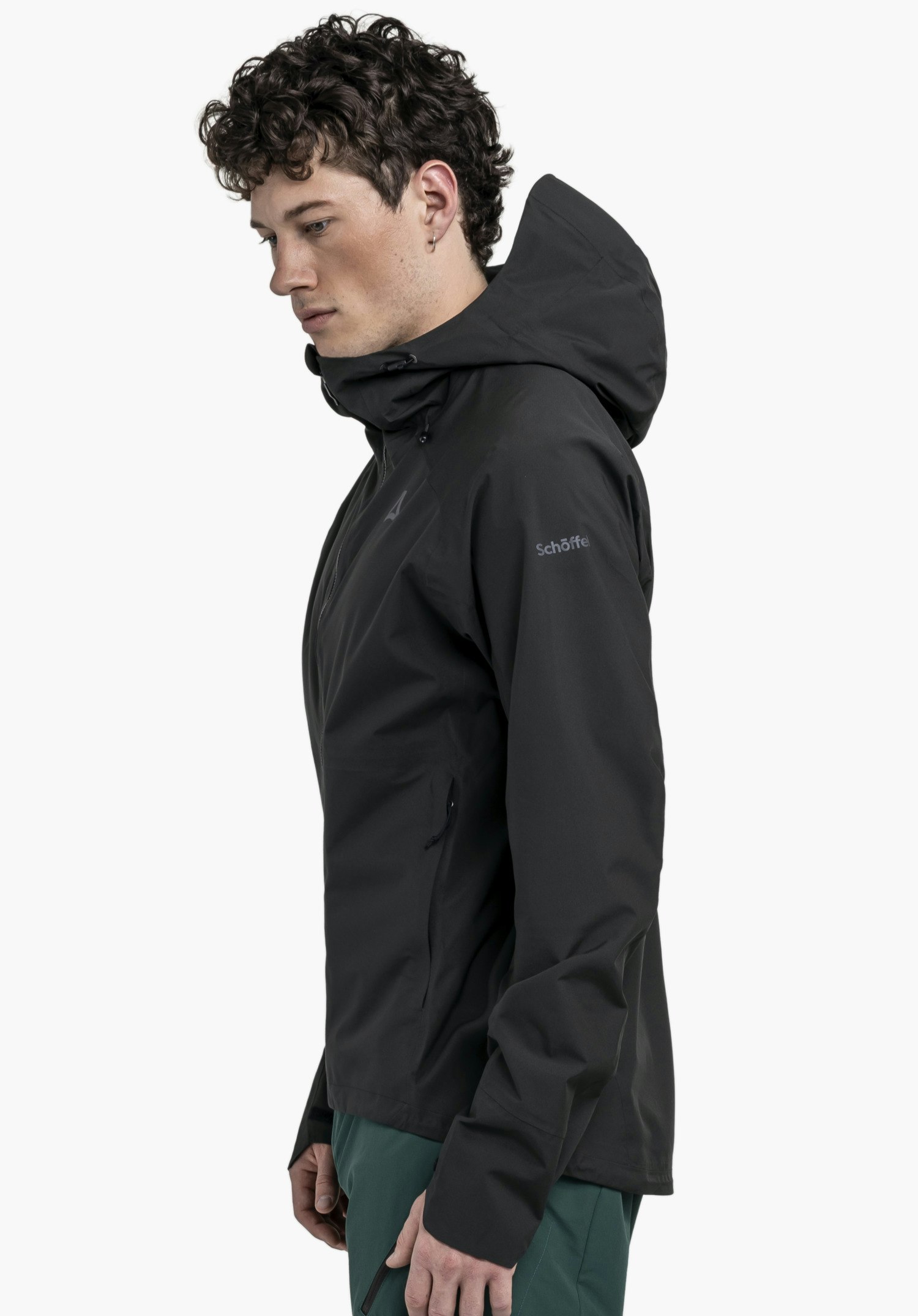 2.5L Jacket Style Tajiva MEN in klassischem Schwarz: Ein Model steht seitlich vor einem neutralen Hintergrund und präsentiert die Passform der Jacke. Das dezente Schöffel-Logo am Oberarm unterstreicht den cleanen Look der Funktionsjacke.
