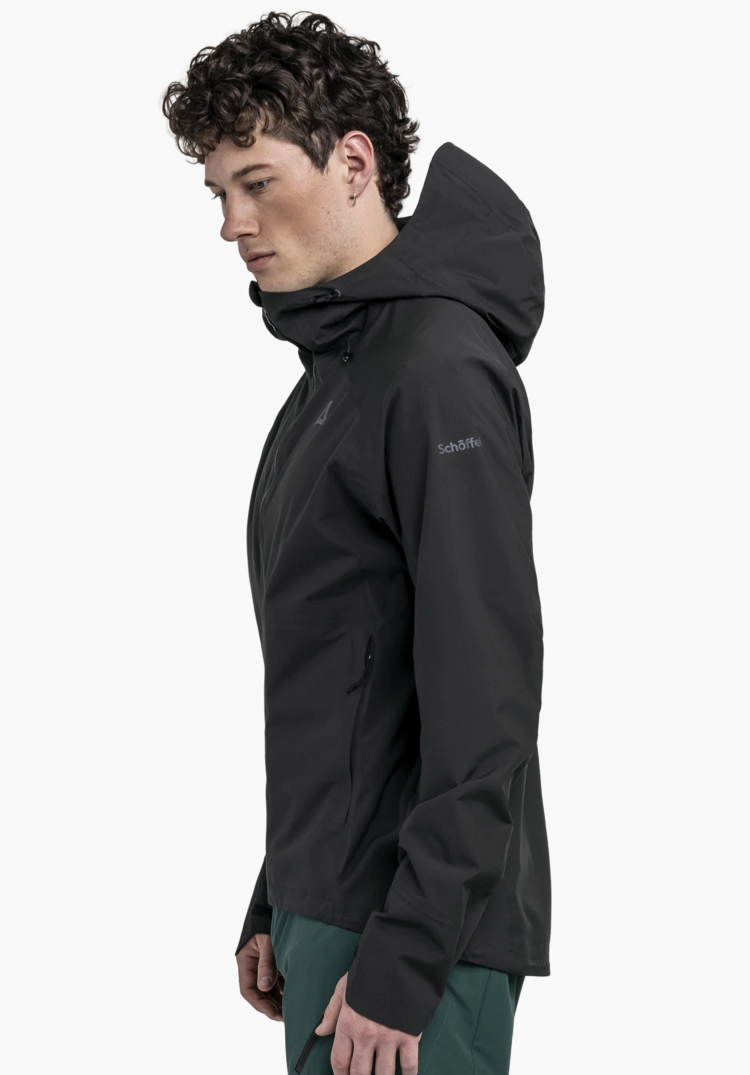 2.5L Jacket Style Tajiva MEN in classic black: A model stands sideways against a neutral background, showcasing the fit of the jacket. The subtle Schöffel logo on the upper arm highlights the clean look of the performance jacket.