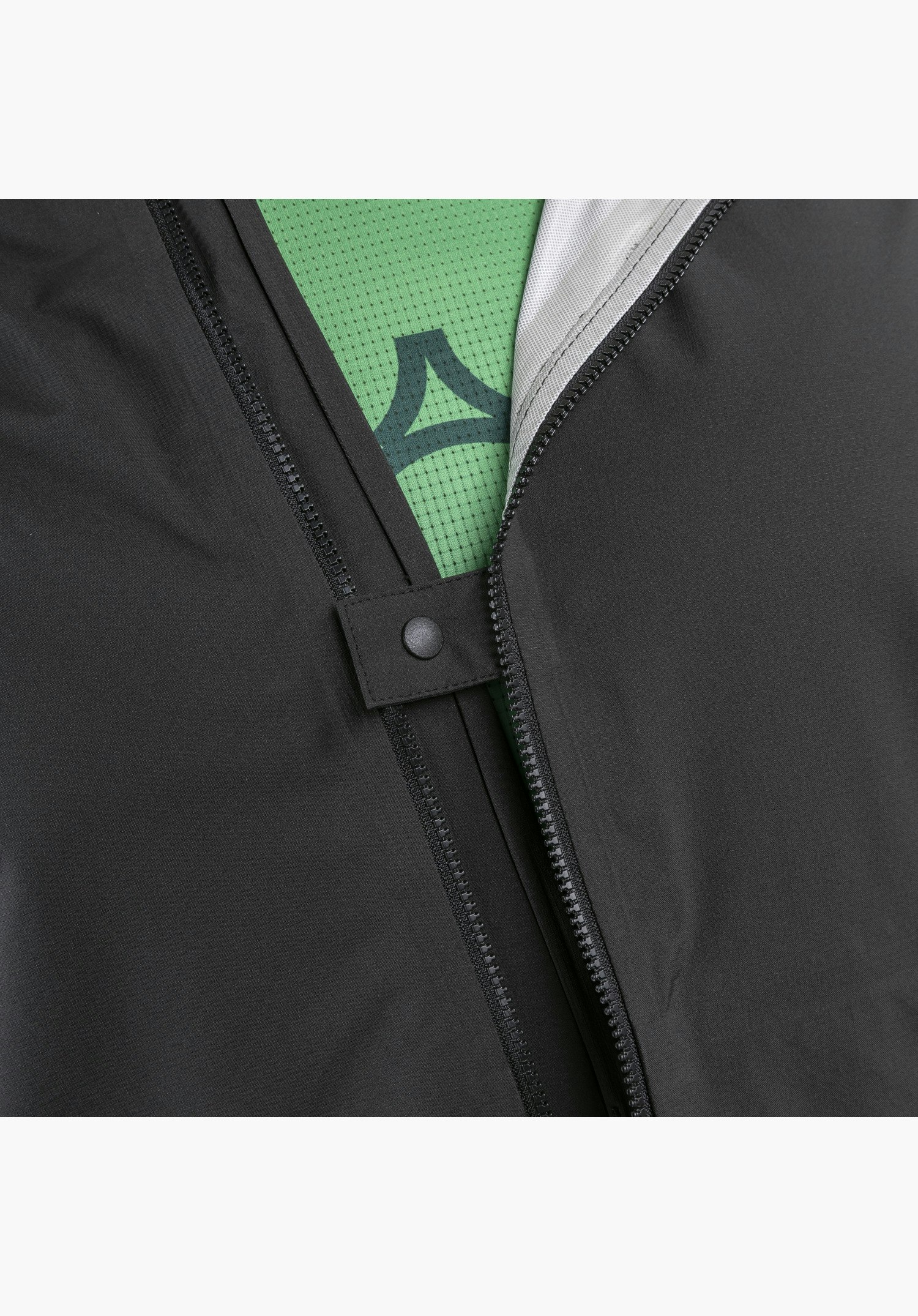 2.5L Jacket Style Tajiva MEN zeigt den teilweise geöffneten, schwarzen Frontreißverschluss mit einer fixierenden Druckknopf-Lasche, wodurch das darunterliegende grüne Material mit Schöffel-Logo sichtbar wird, als Nahaufnahme vor weißem Hintergrund.