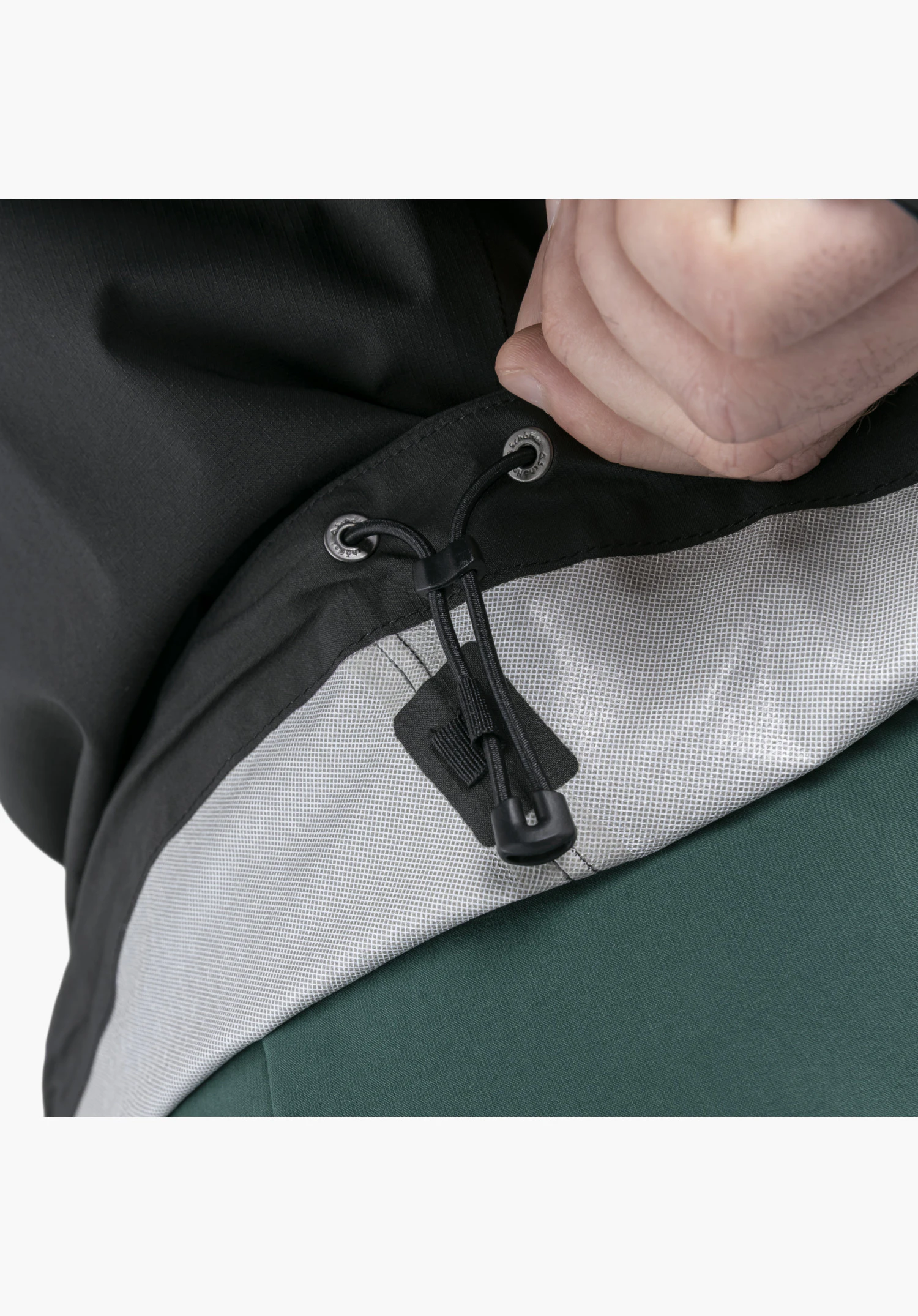 2.5L Jacket Style Tajiva MEN features a detailed view of the adjustable black drawcord with a toggle and eyelets bearing the Schöffel-Logo at the hem, gripped by a hand to reveal the light inner lining, as a close-up against a white/neutral background.