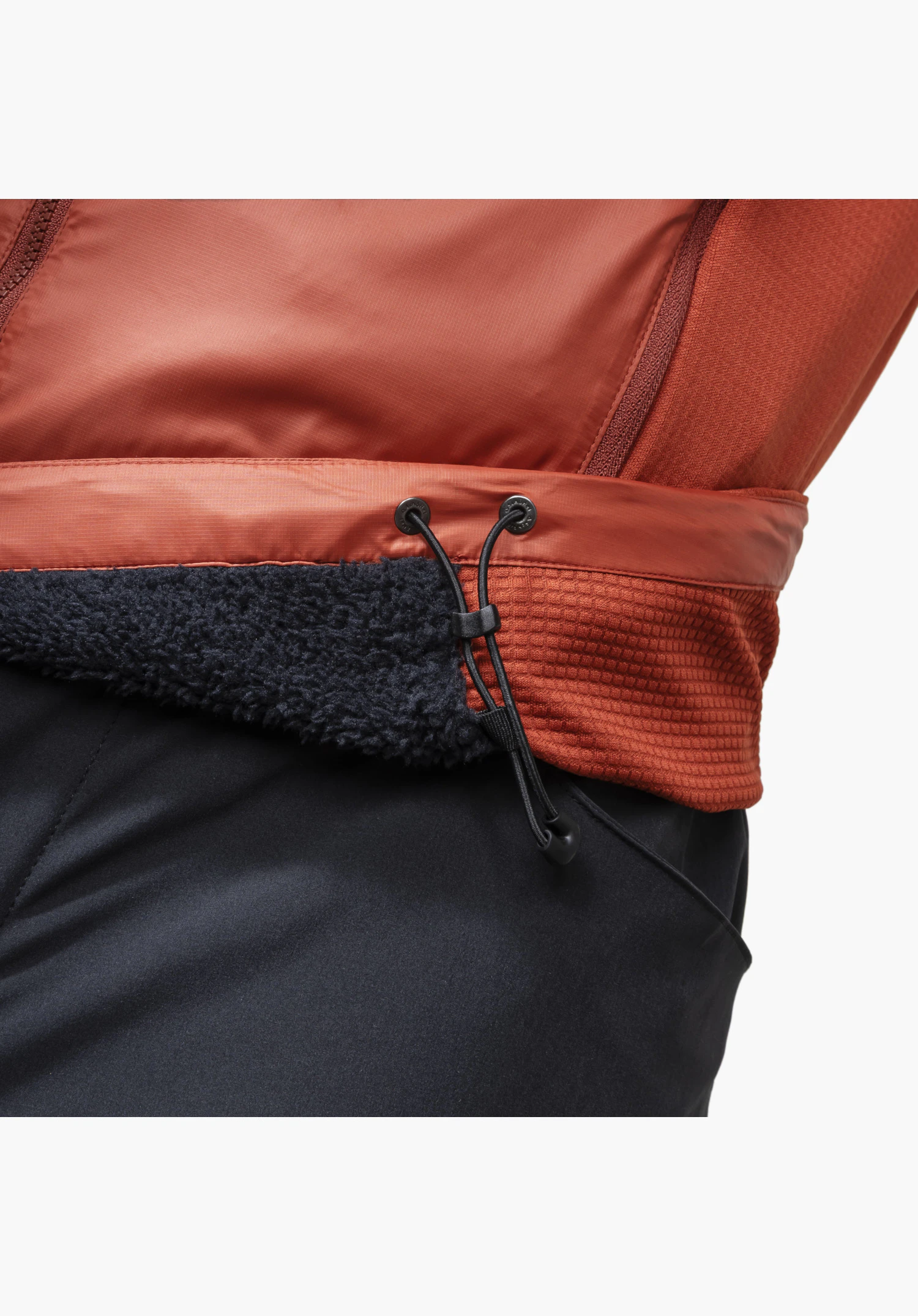 Ins Jacket Style Samaia MEN, vue détaillée du cordon de serrage réglable à l'ourlet, associé à un tissu rouge texturé et lisse ainsi qu'à une doublure intérieure en polaire noire apparente, gros plan sur fond blanc/neutre.