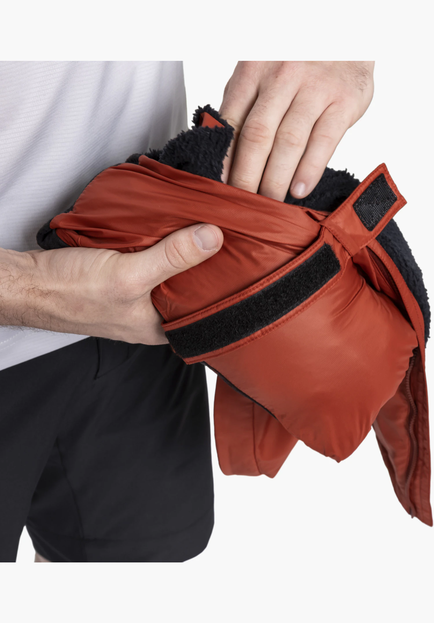Ins Jacket Style Samaia MEN avec un accent sur la large fermeture auto-agrippante et la douce doublure en polaire noire sur le tissu rouge, tenus par des mains d'homme. Gros plan sur fond blanc/neutre.
