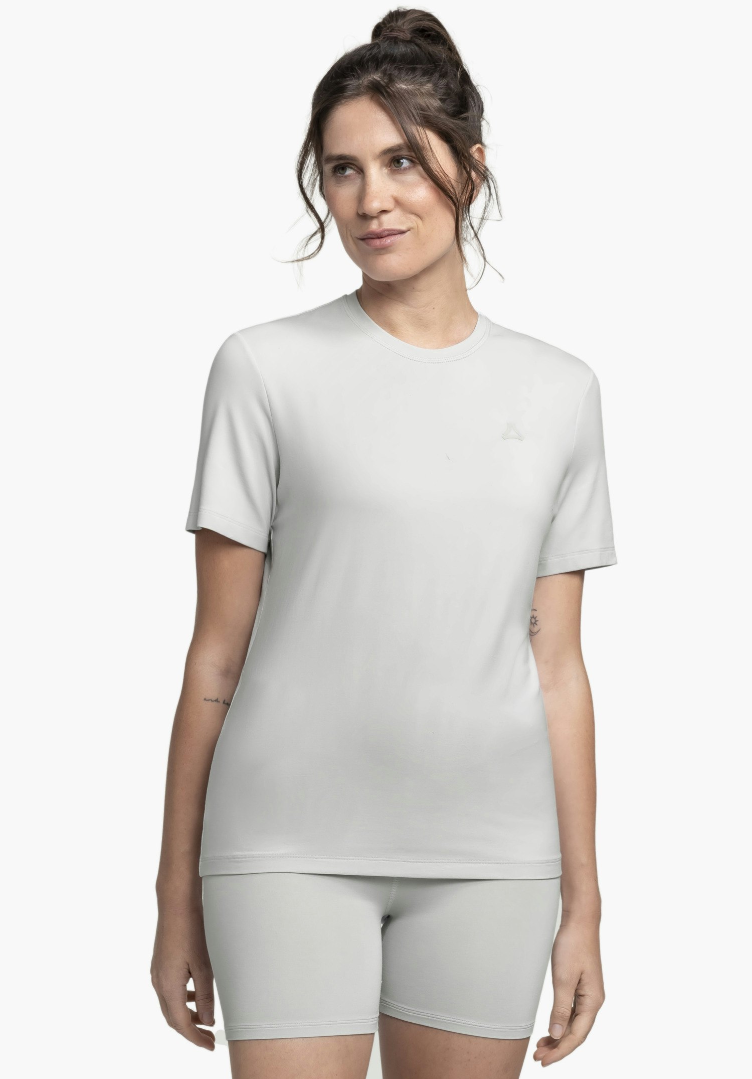 T Shirt Style Mafadi WMN est porté par un mannequin qui se tient de face et regarde légèrement sur le côté. Le t-shirt gris à manches courtes présente un logo Schöffel discret sur la poitrine gauche et est présenté sur un fond neutre.