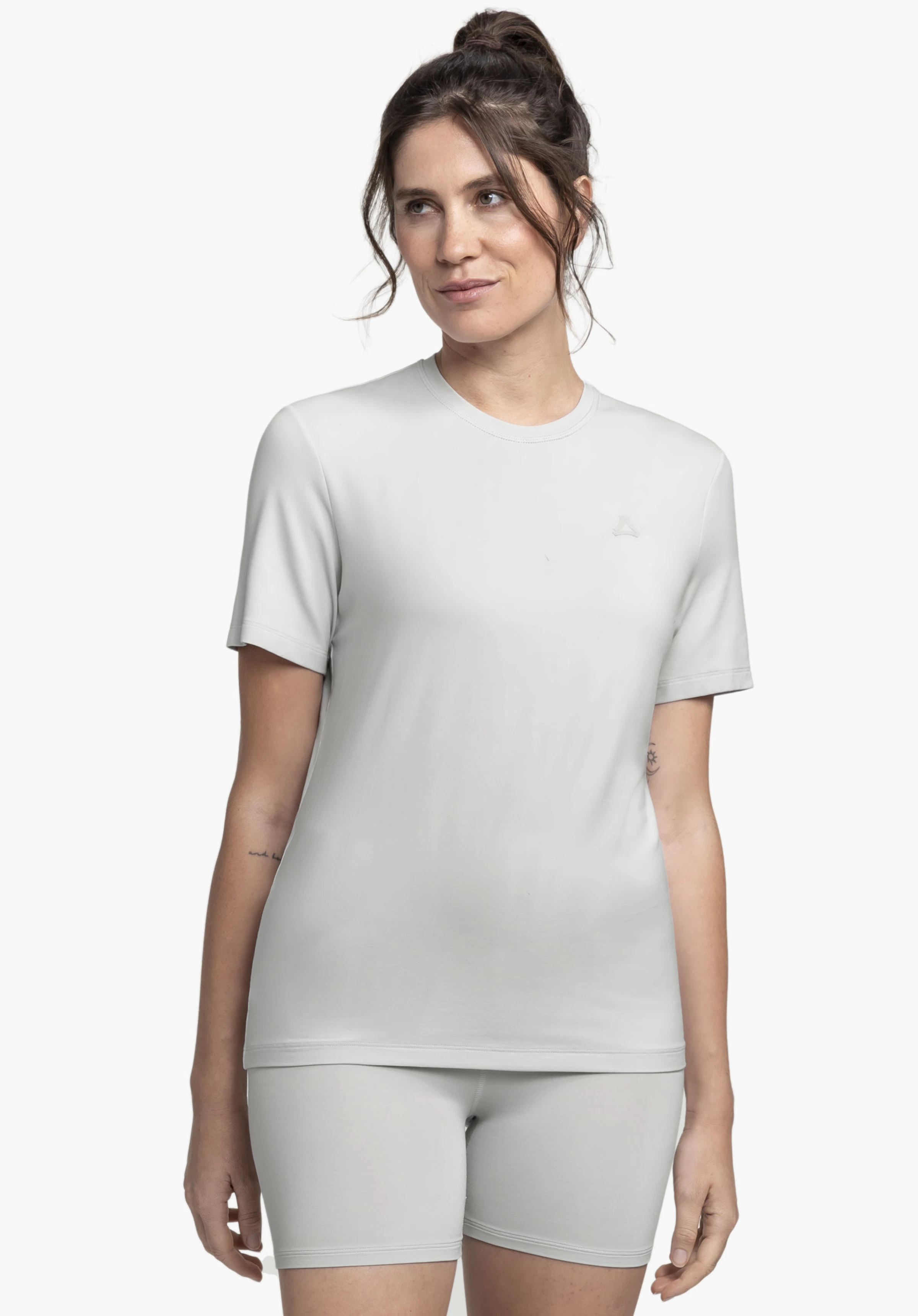 T Shirt Style Mafadi WMN est porté par un mannequin qui se tient de face et regarde légèrement sur le côté. Le t-shirt gris à manches courtes présente un logo Schöffel discret sur la poitrine gauche et est présenté sur un fond neutre.