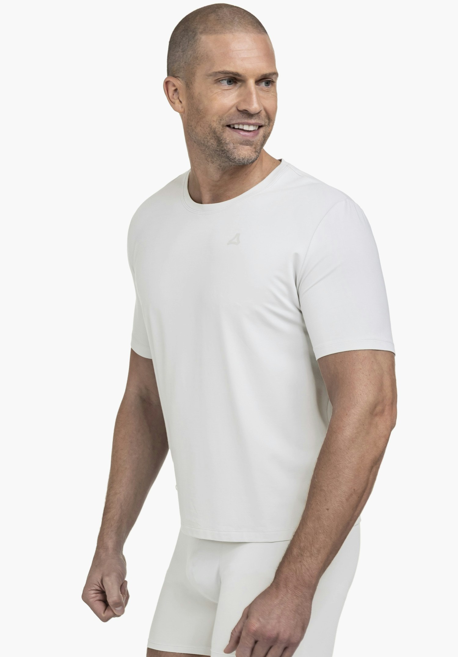 T Shirt Style Mafadi MEN in Grau: Ein Model steht in Halbprofil-Pose vor einem neutralen Hintergrund und blickt leicht zur Seite. Das schlichte Shirt unterstreicht die sportliche Silhouette, wobei das dezente Schöffel-Logo auf der Brust das Design perfekt abrundet.
