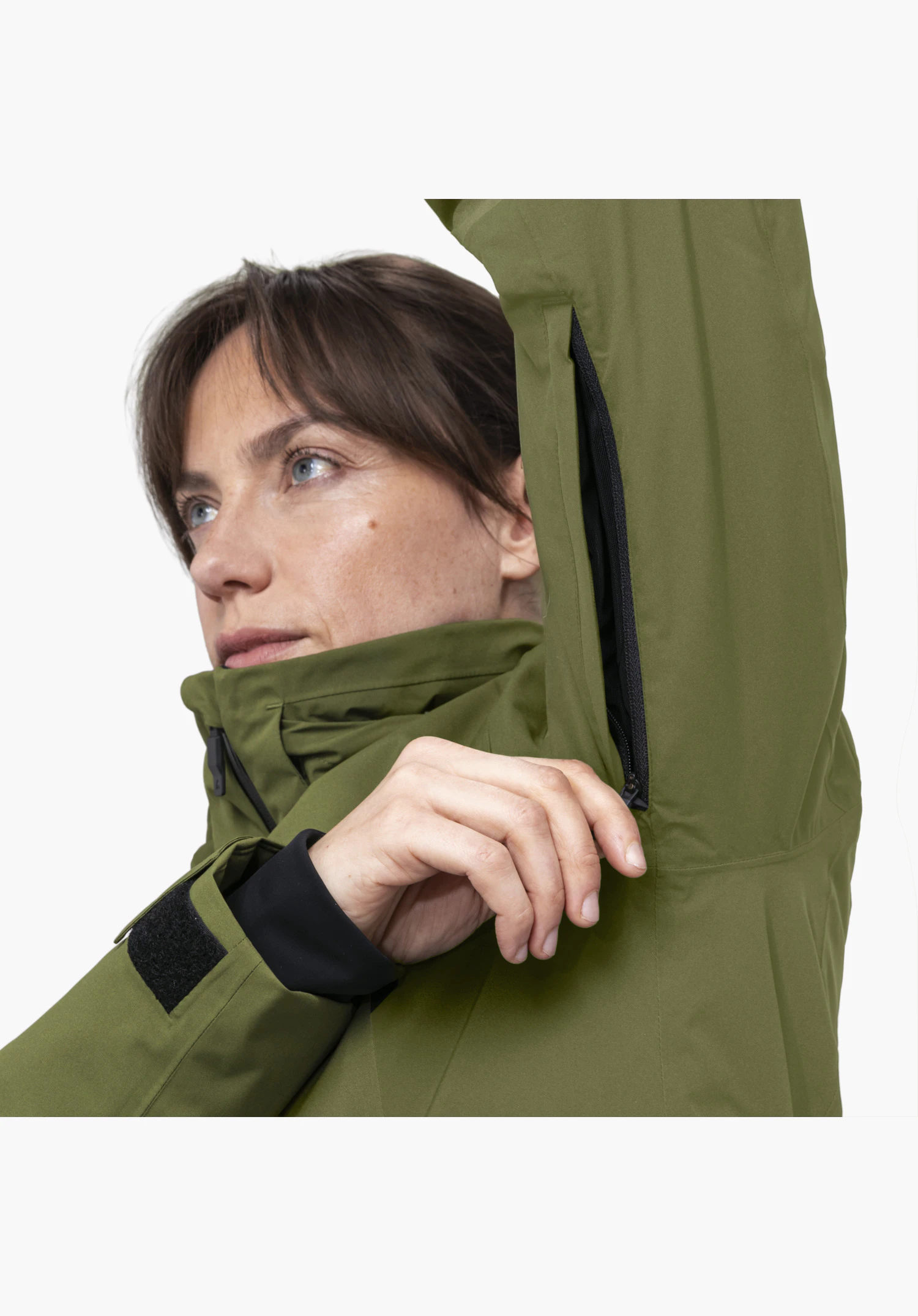 Jacket Style Trifex WMN en vert avec focus sur l'ouverture de ventilation zippée sous le bras, manipulée par une personne de sexe féminin. Vue en gros plan sur fond blanc.